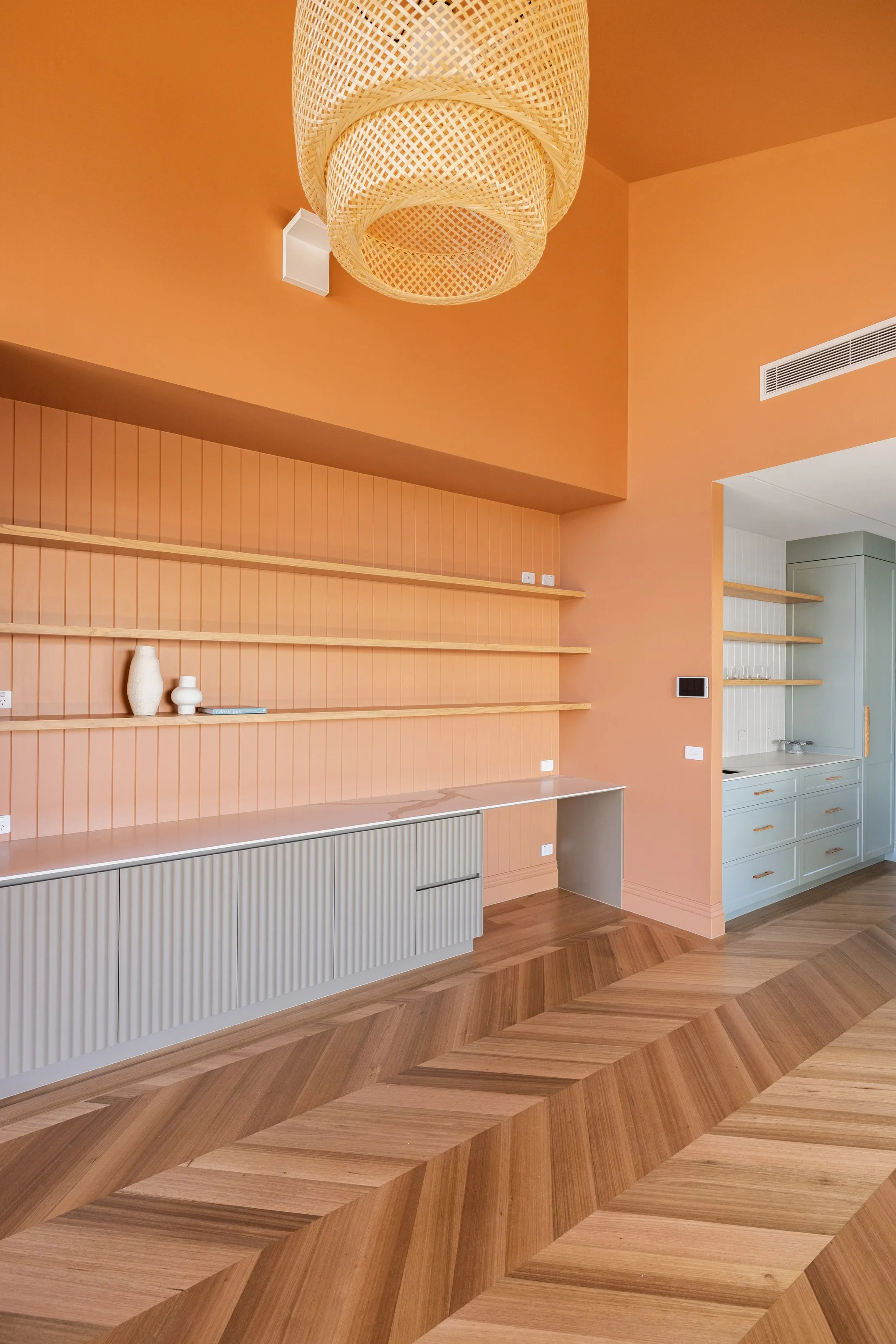 Woven rattan pendant above a panelled study nook, terracotta walls meeting chevron parquet