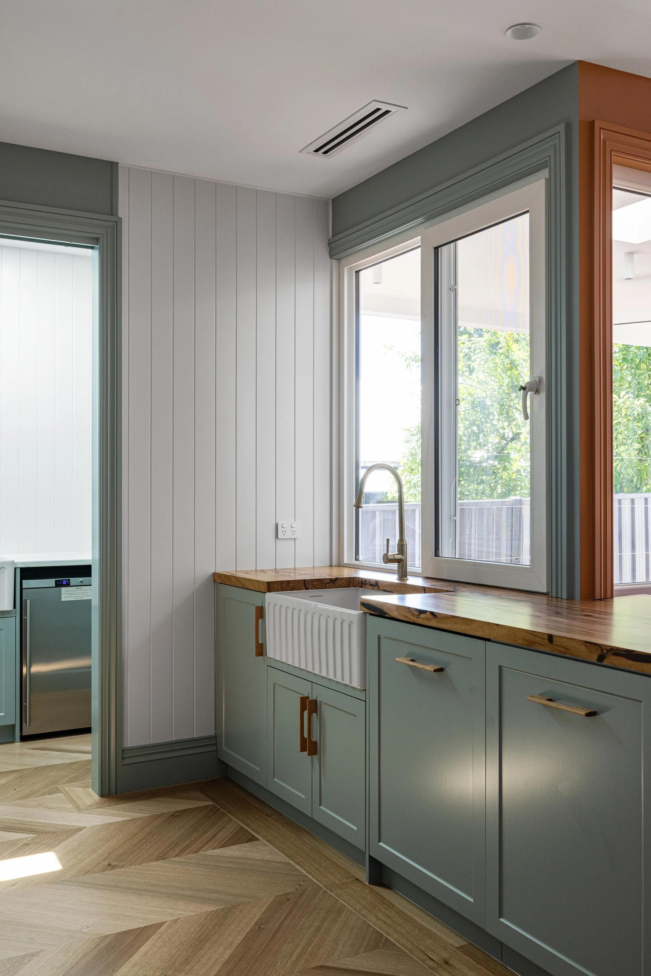 Timber benchtop and fluted apron sink in sage joinery, with a window above and VJ panelled wall