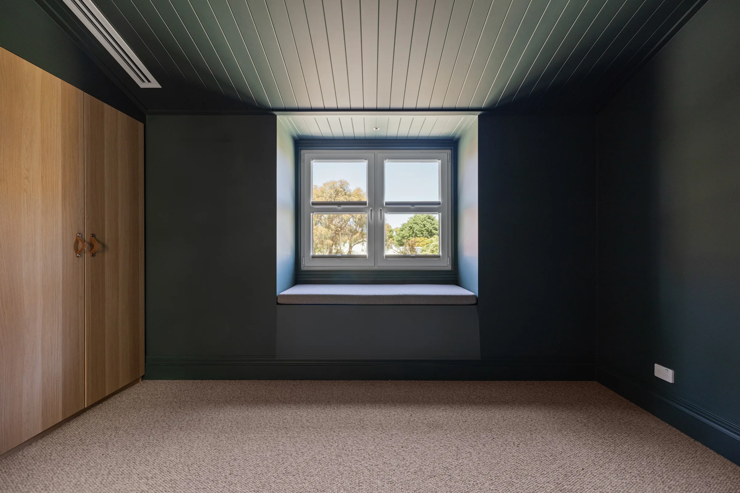 Bedroom in deep charcoal blue with a lined timber ceiling, window seat and timber wardrobe doors