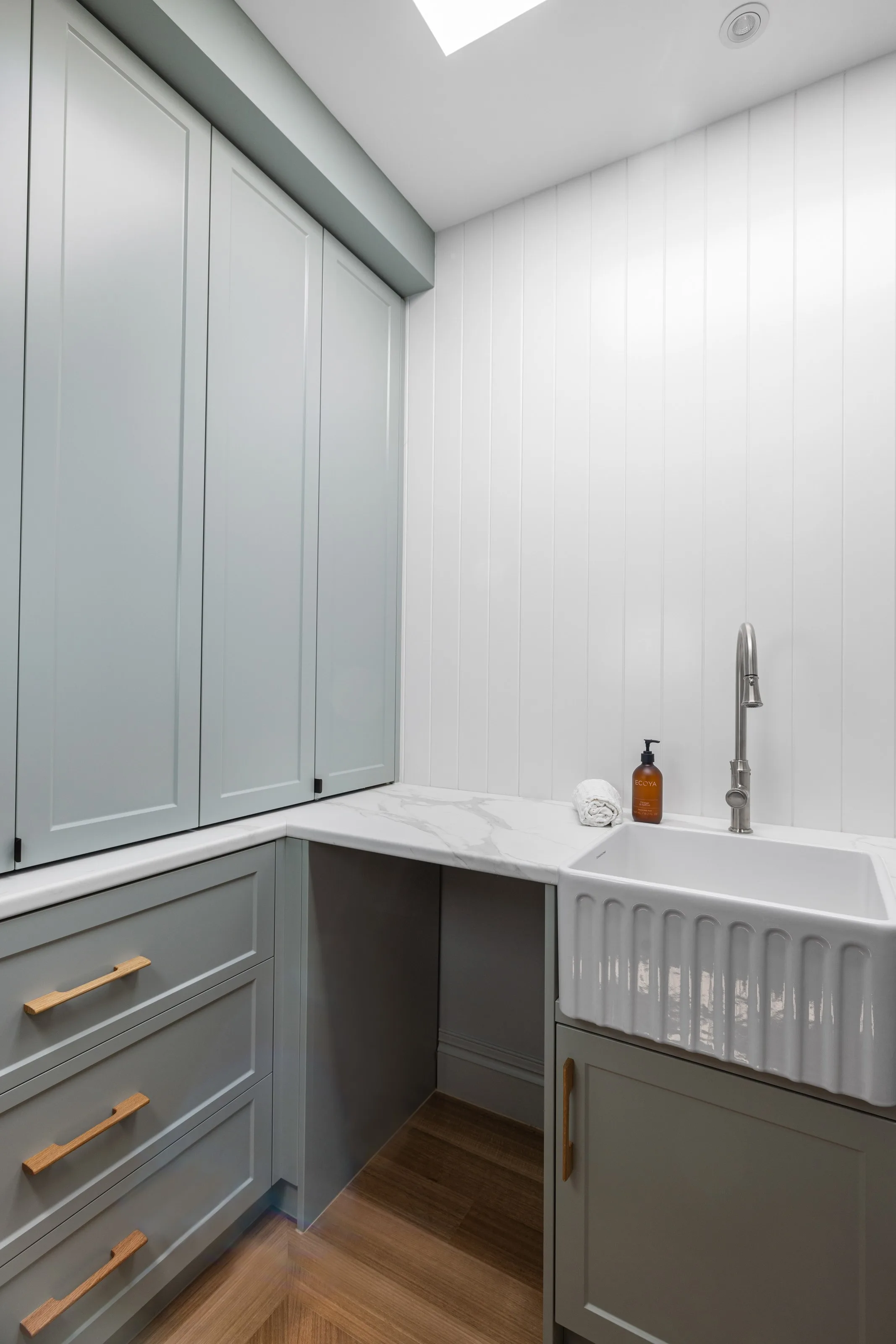 Tall pale grey pantry joinery under a skylight, with stone benchtop and fluted apron sink