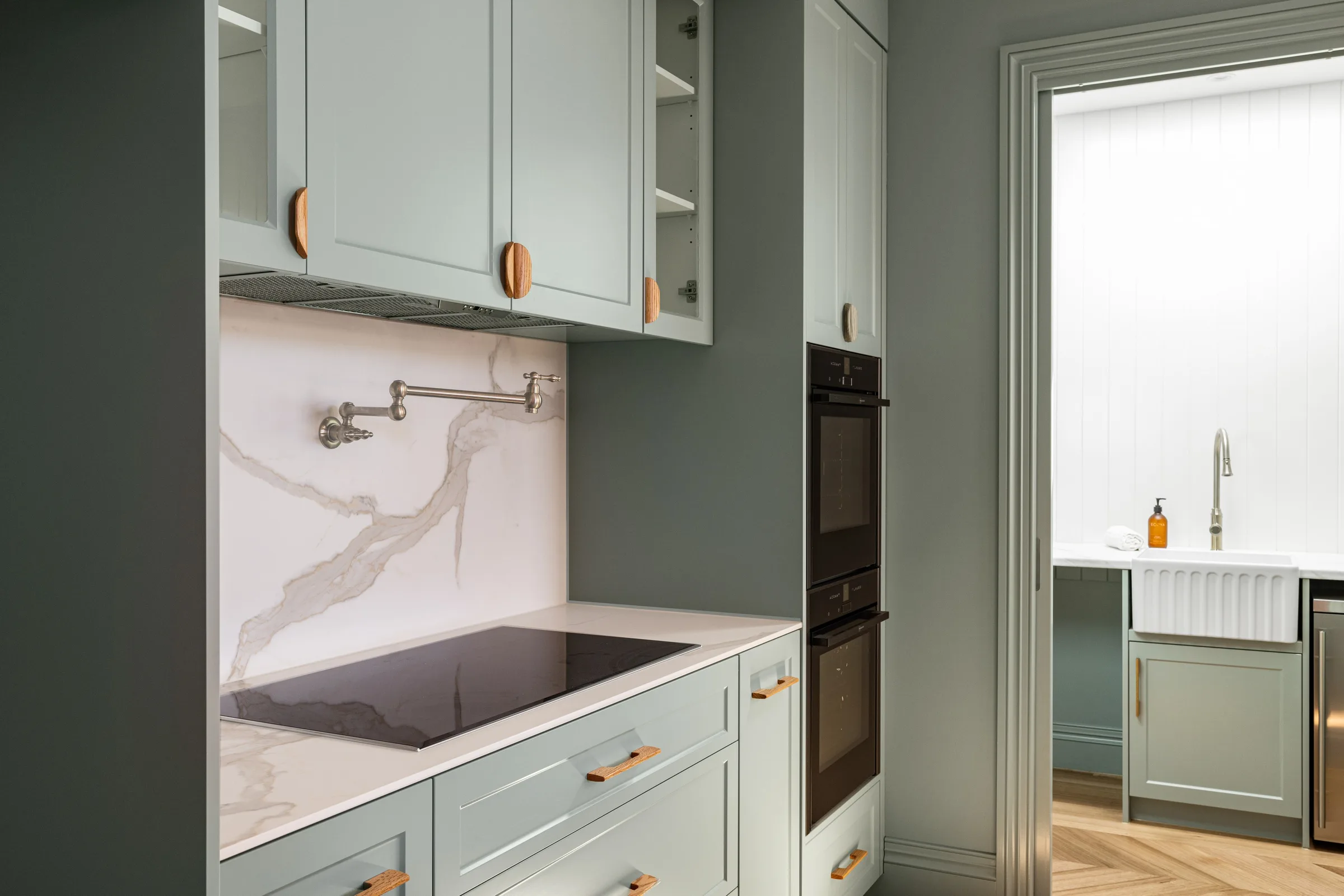 Veined stone splashback with a wall-mounted pot filler above the cooktop, sage joinery either side
