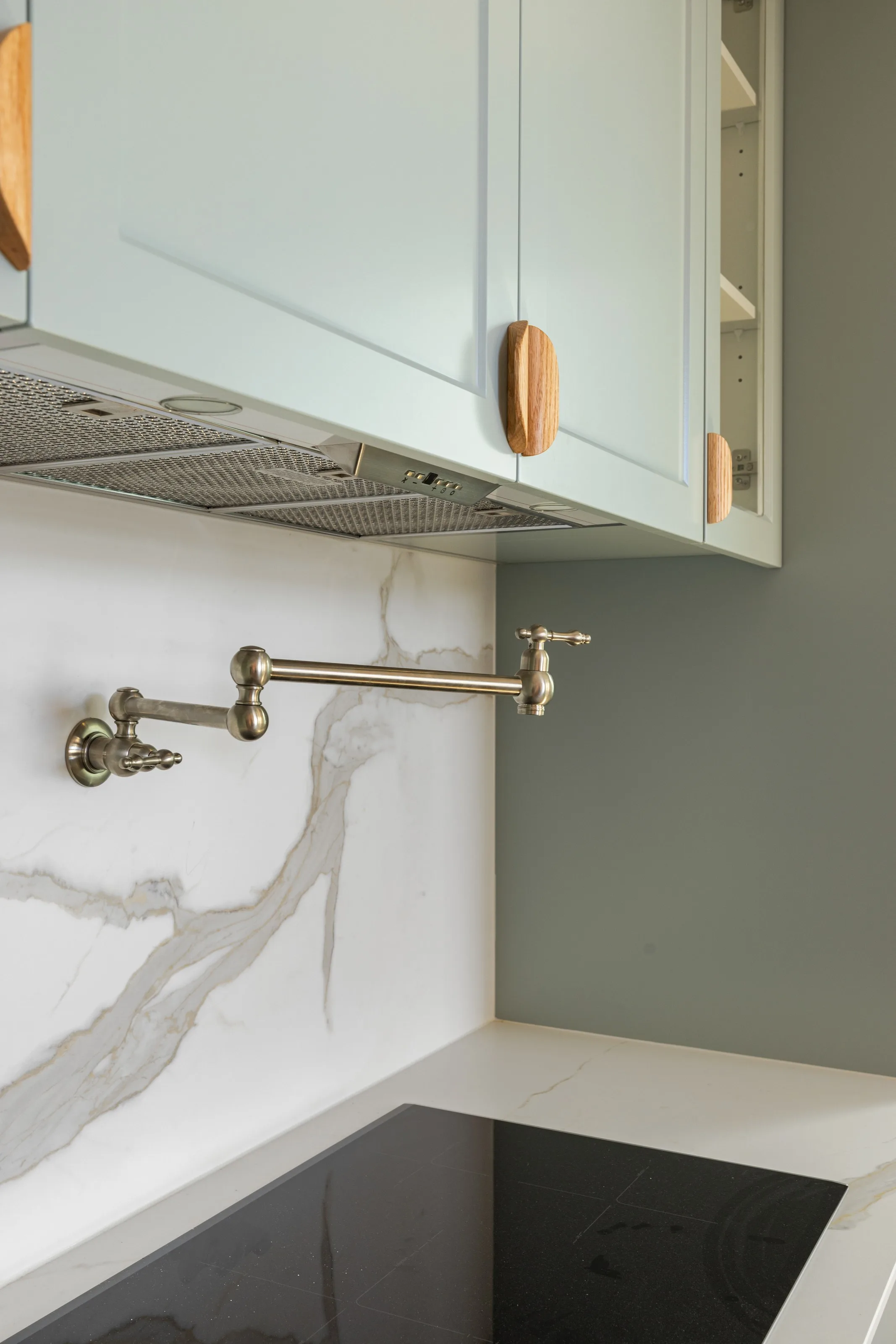 Brushed nickel pot filler and concealed rangehood against a veined stone splashback