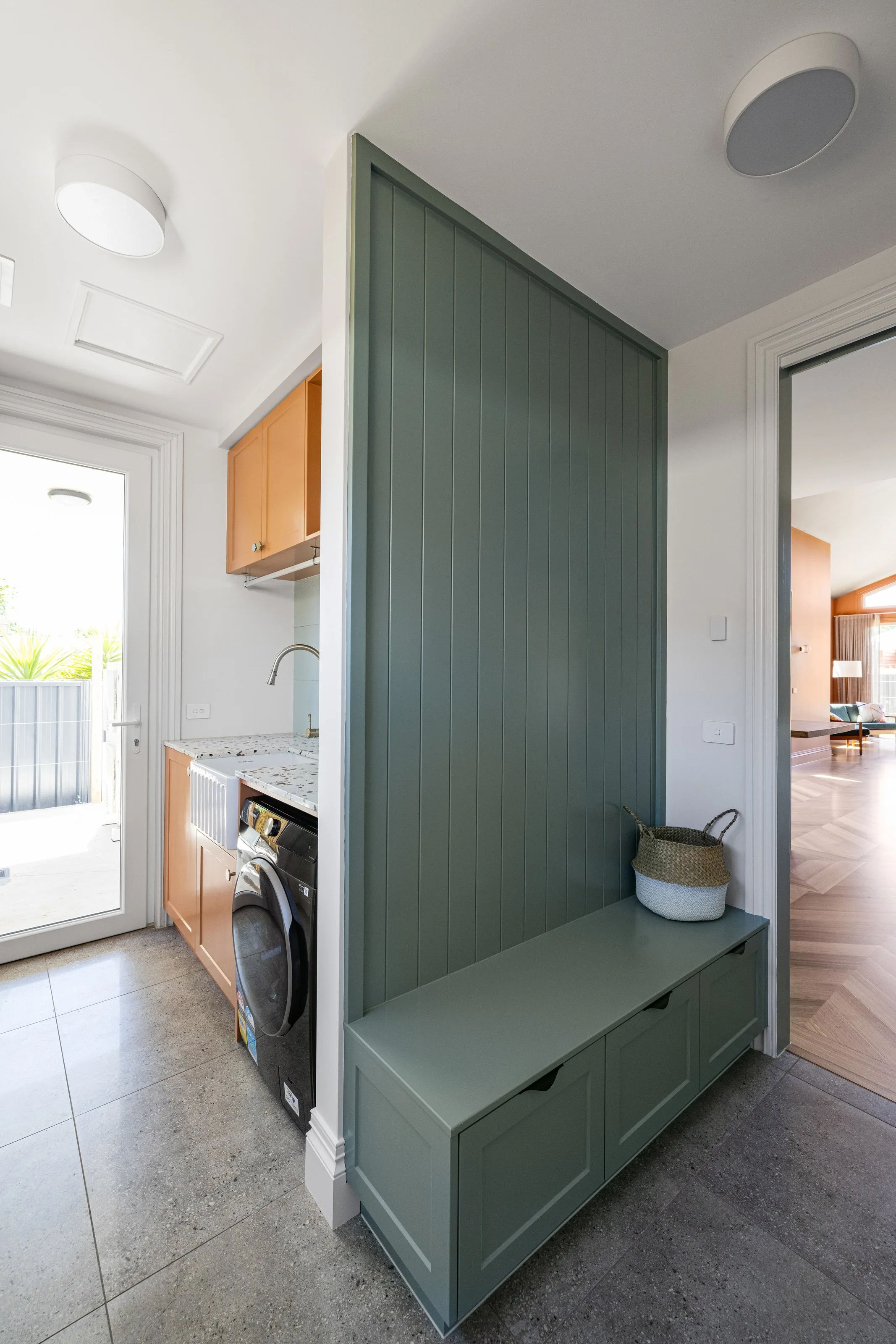 Mudroom bench seat with drawers against green VJ panelling, laundry joinery and tiled floor beyond