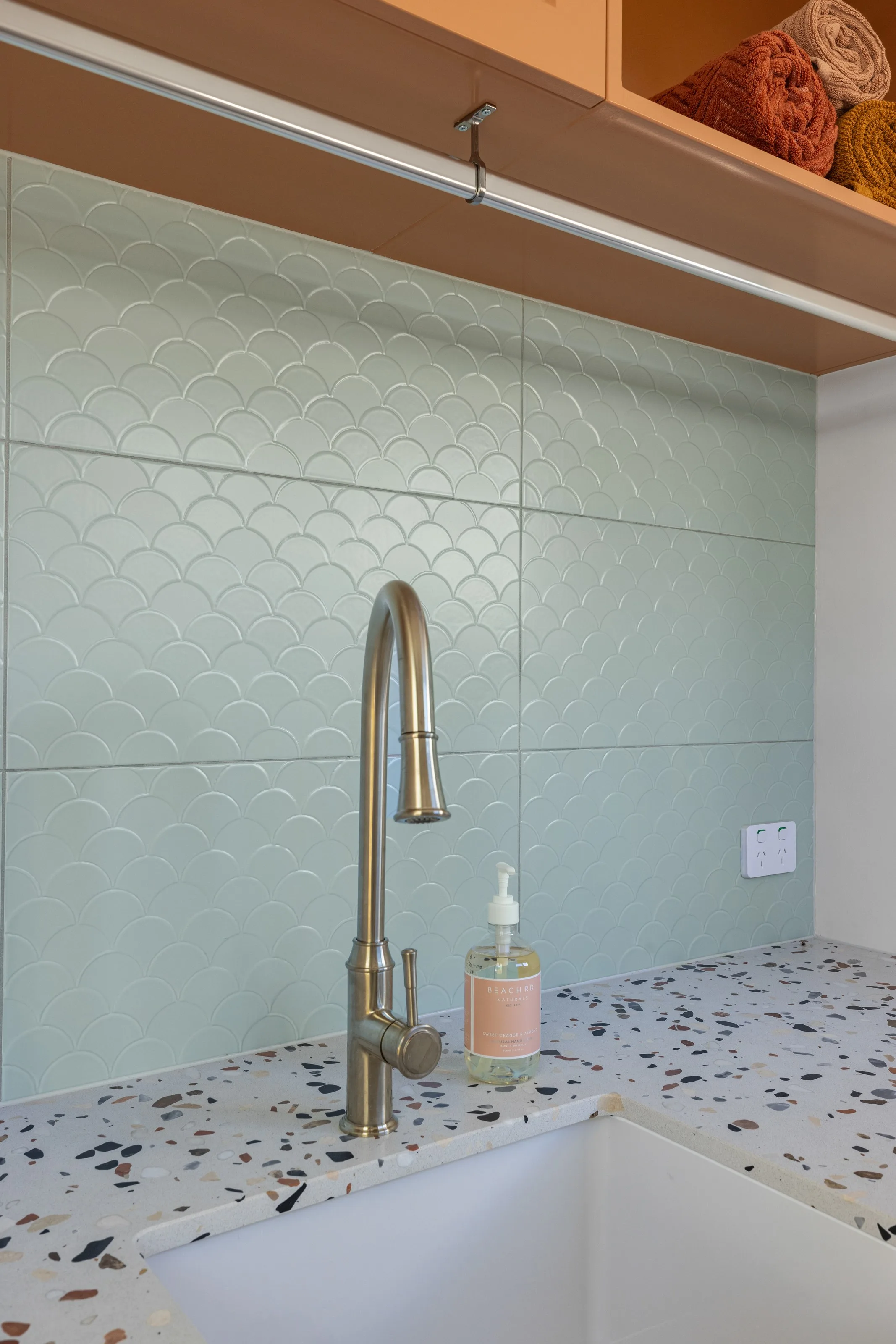 Mint scalloped tiles behind a terrazzo benchtop, brushed nickel tapware and terracotta overhead joinery