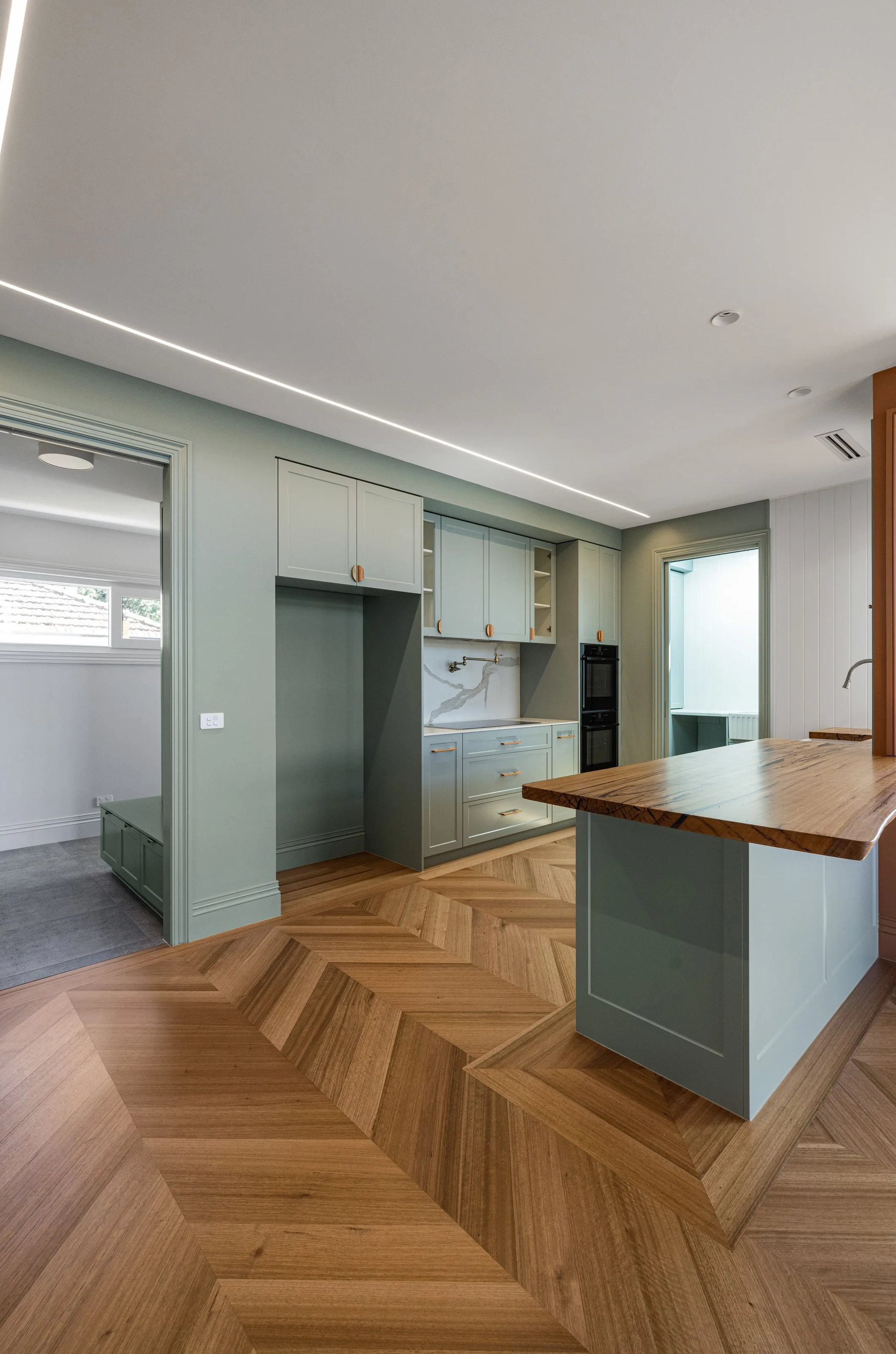 Warren St kitchen with sage joinery and a timber-topped island, chevron parquet running through