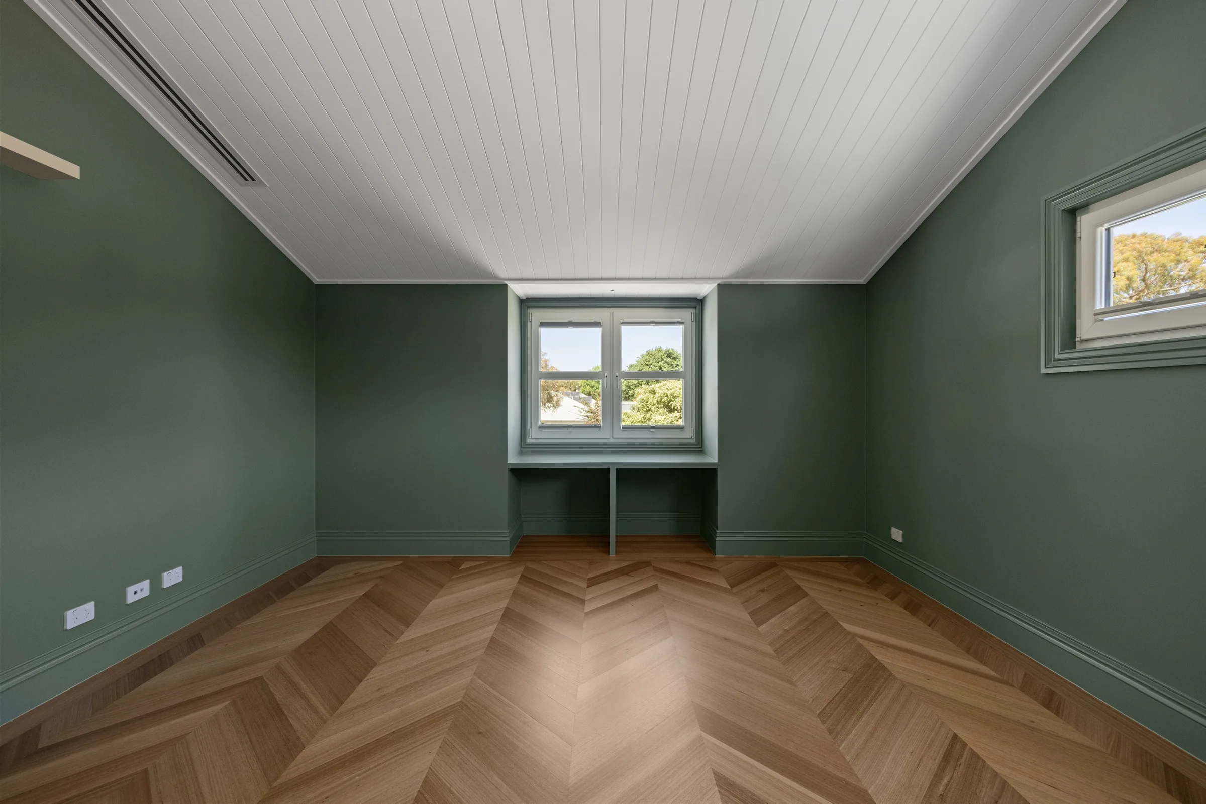 Bedroom in deep green with a white lined ceiling and a built-in desk beneath the window