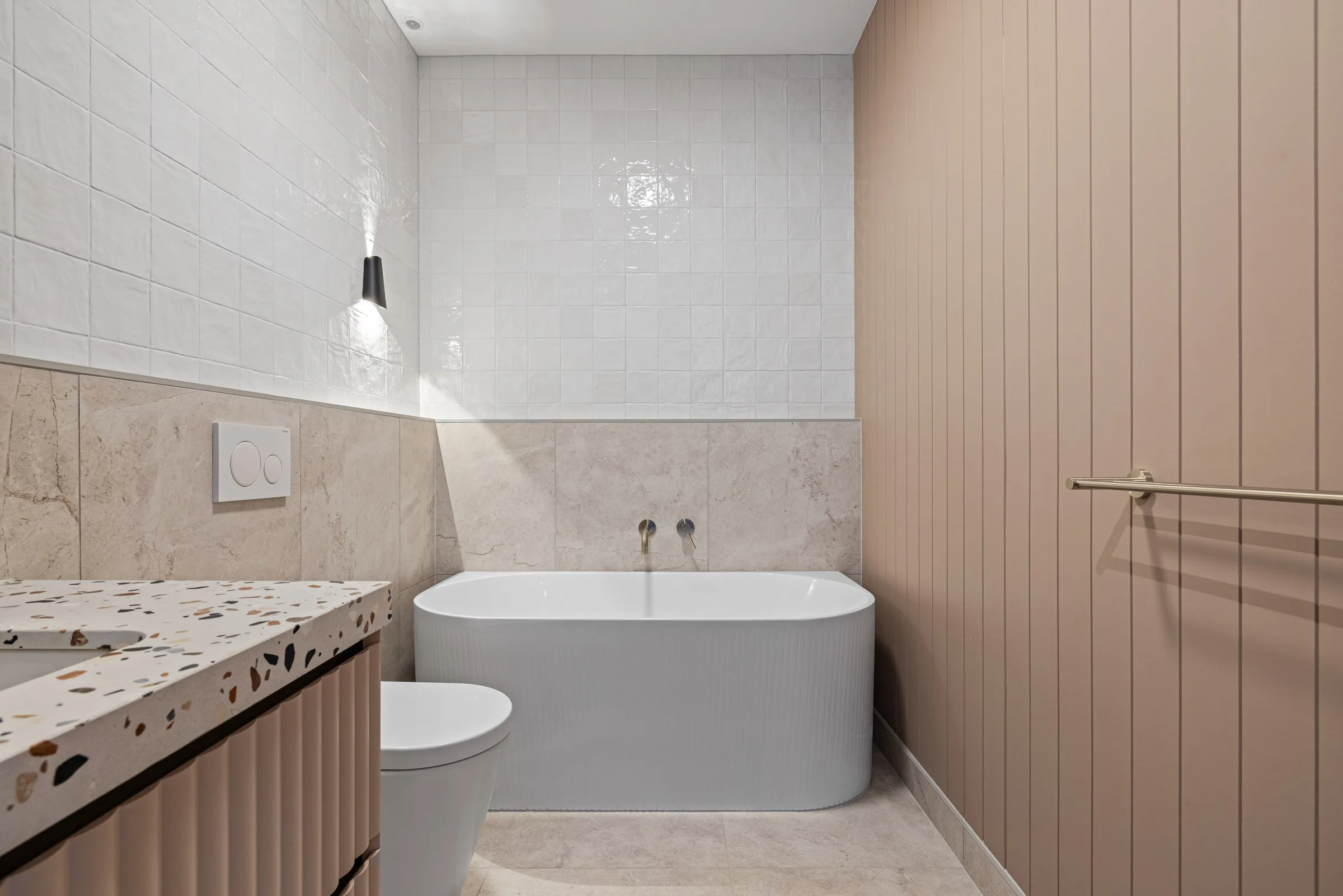 Freestanding oval bath against blush VJ panelling, with square gloss tiles and a fluted vanity