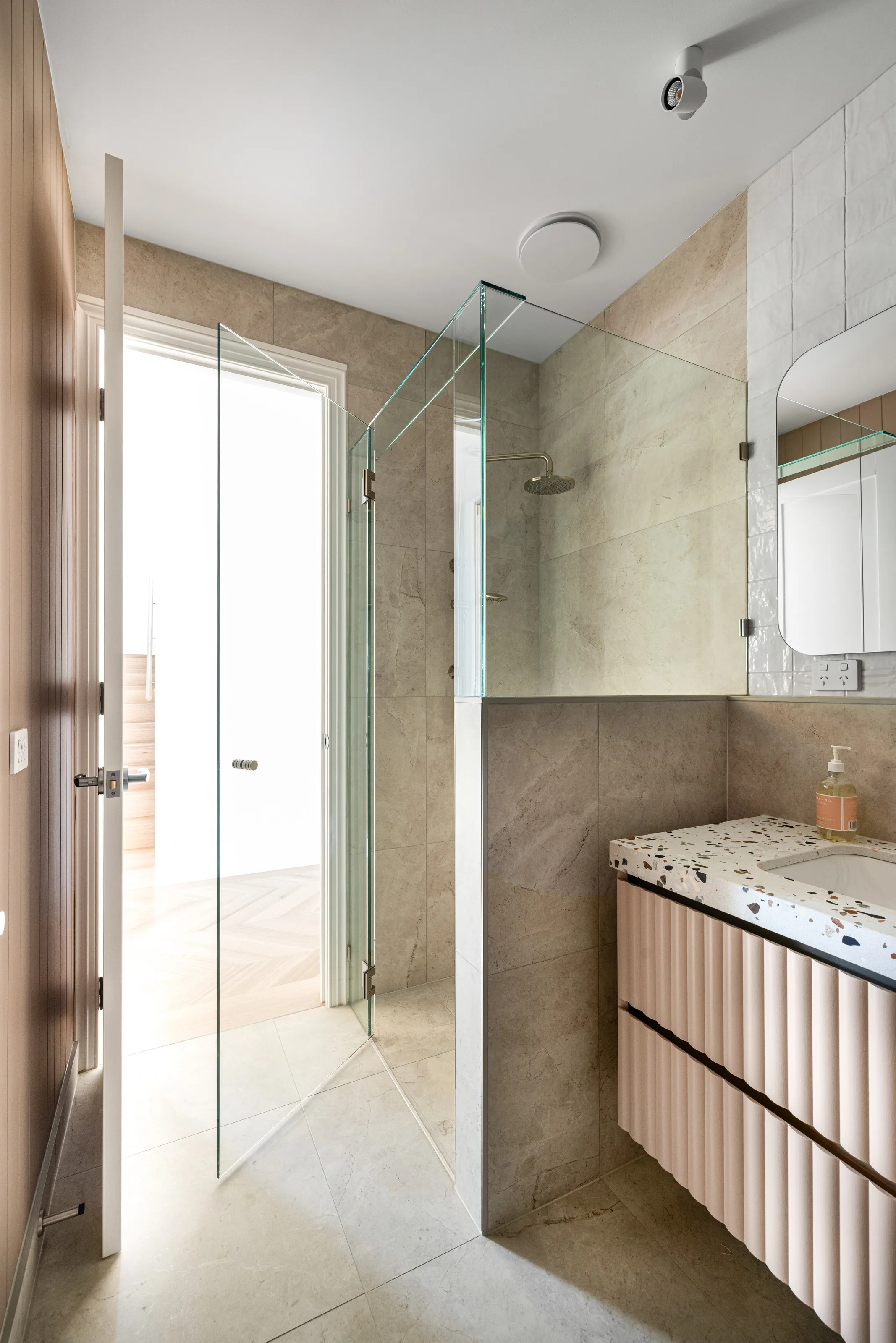 Bathroom looking through to the hall, glazed shower screen beside a fluted blush vanity