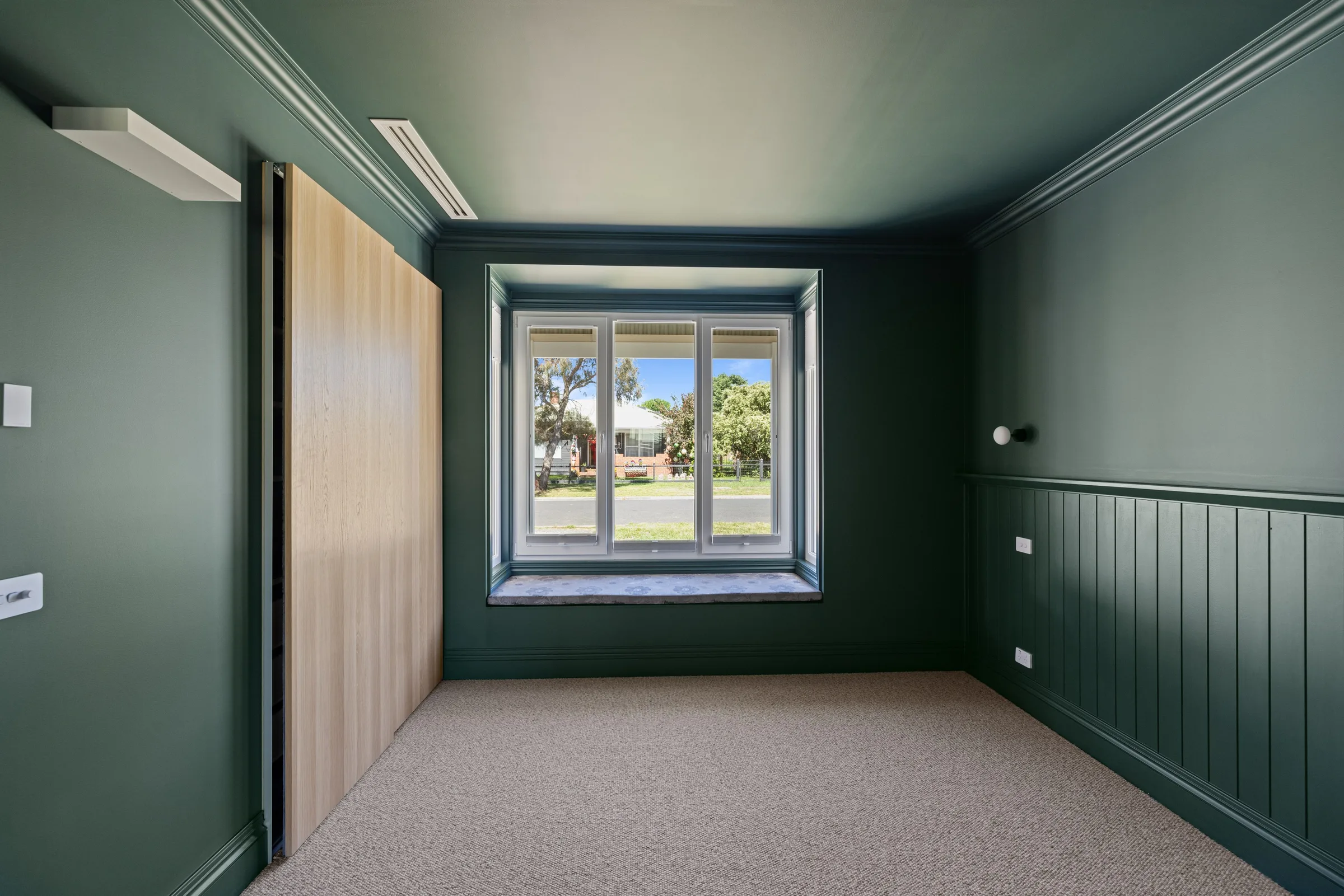 Dark green bedroom with panelled wainscoting, timber wardrobe doors and a window seat
