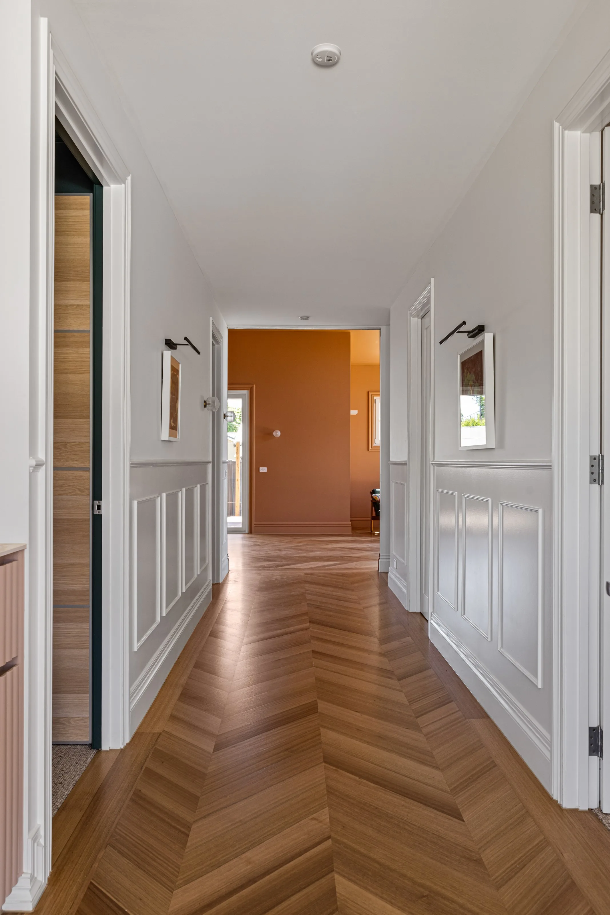 Wainscoted hall with framed artwork, a timber cavity slider and chevron parquet underfoot