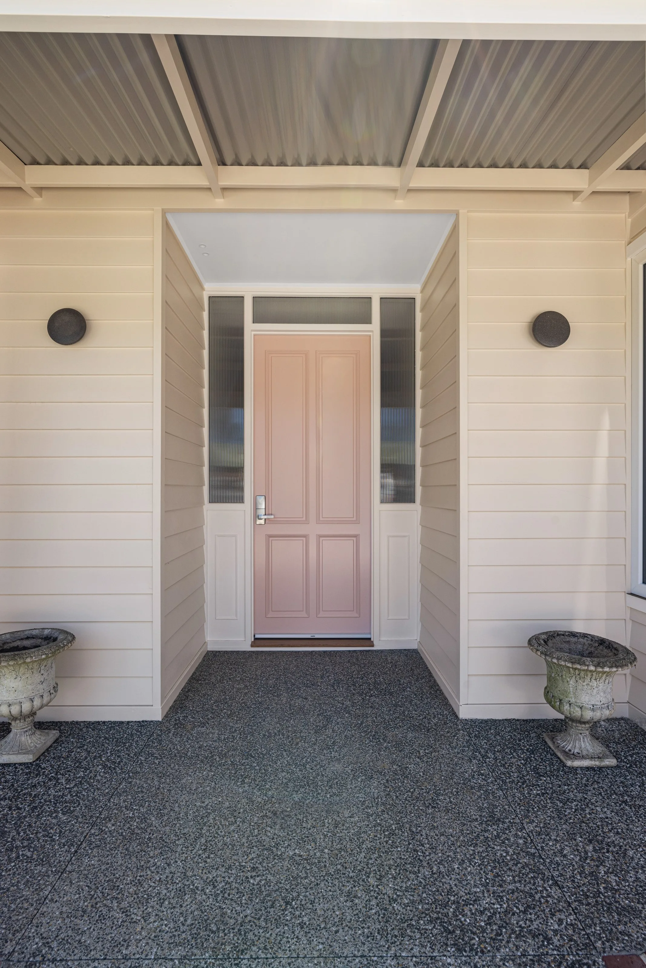 Blush panelled front door with sidelights, cream weatherboards and urn planters on the porch