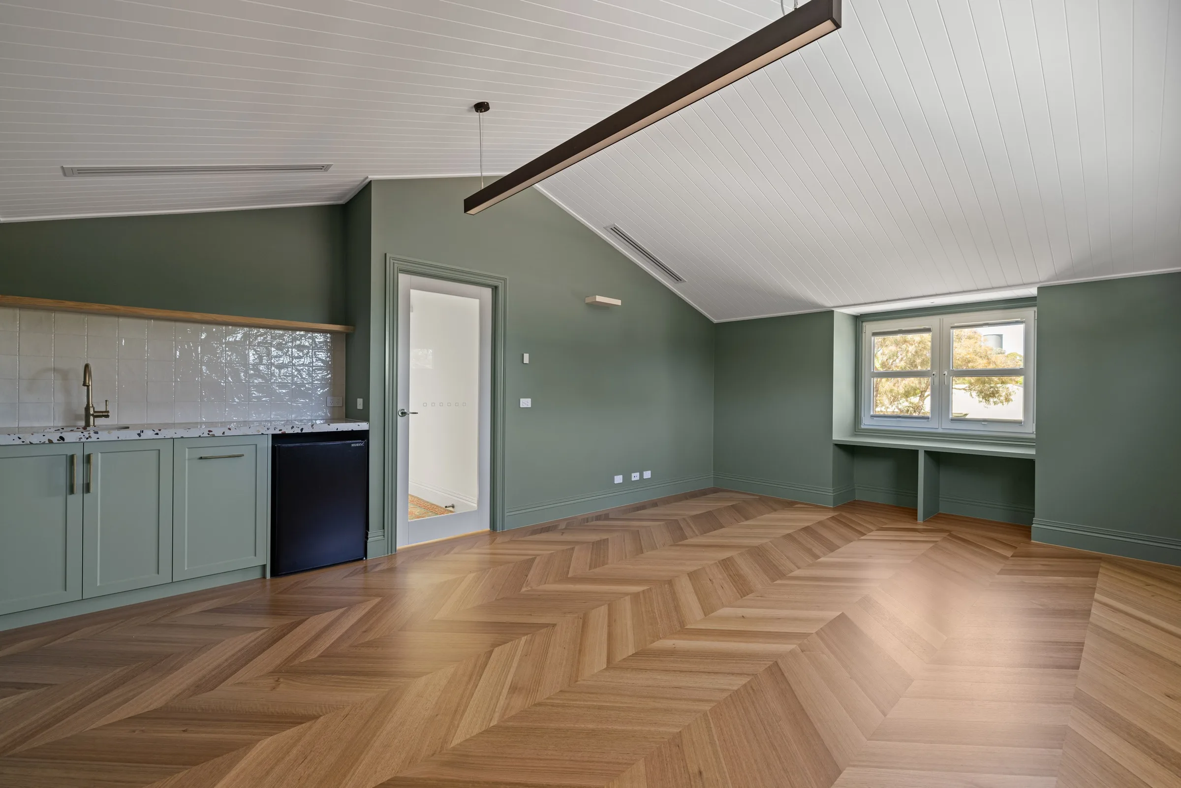 Upstairs living room with sage walls, a raked lined ceiling, kitchenette and built-in window desk