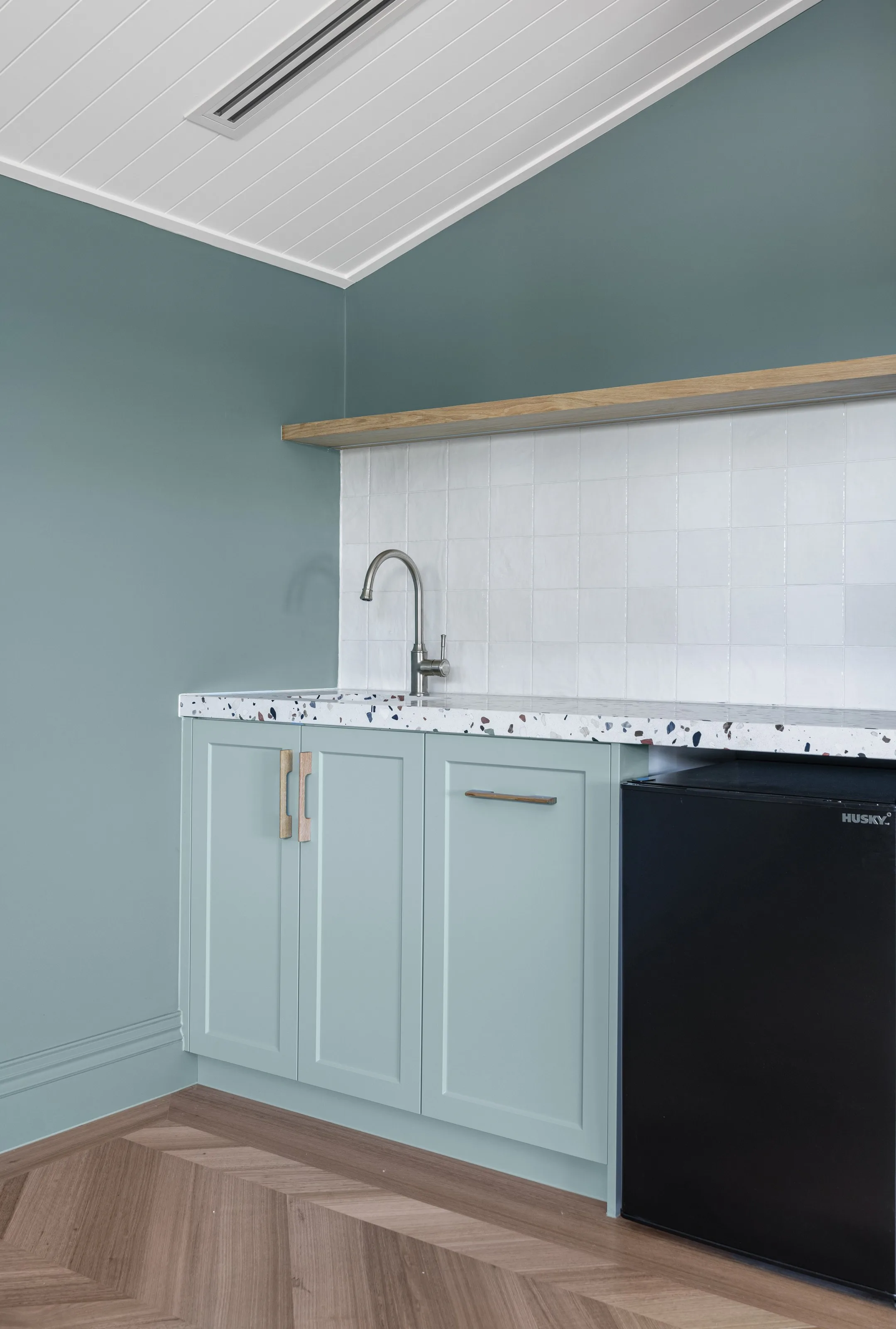 Kitchenette with pale blue-green shaker joinery, terrazzo benchtop and square white tiled splashback