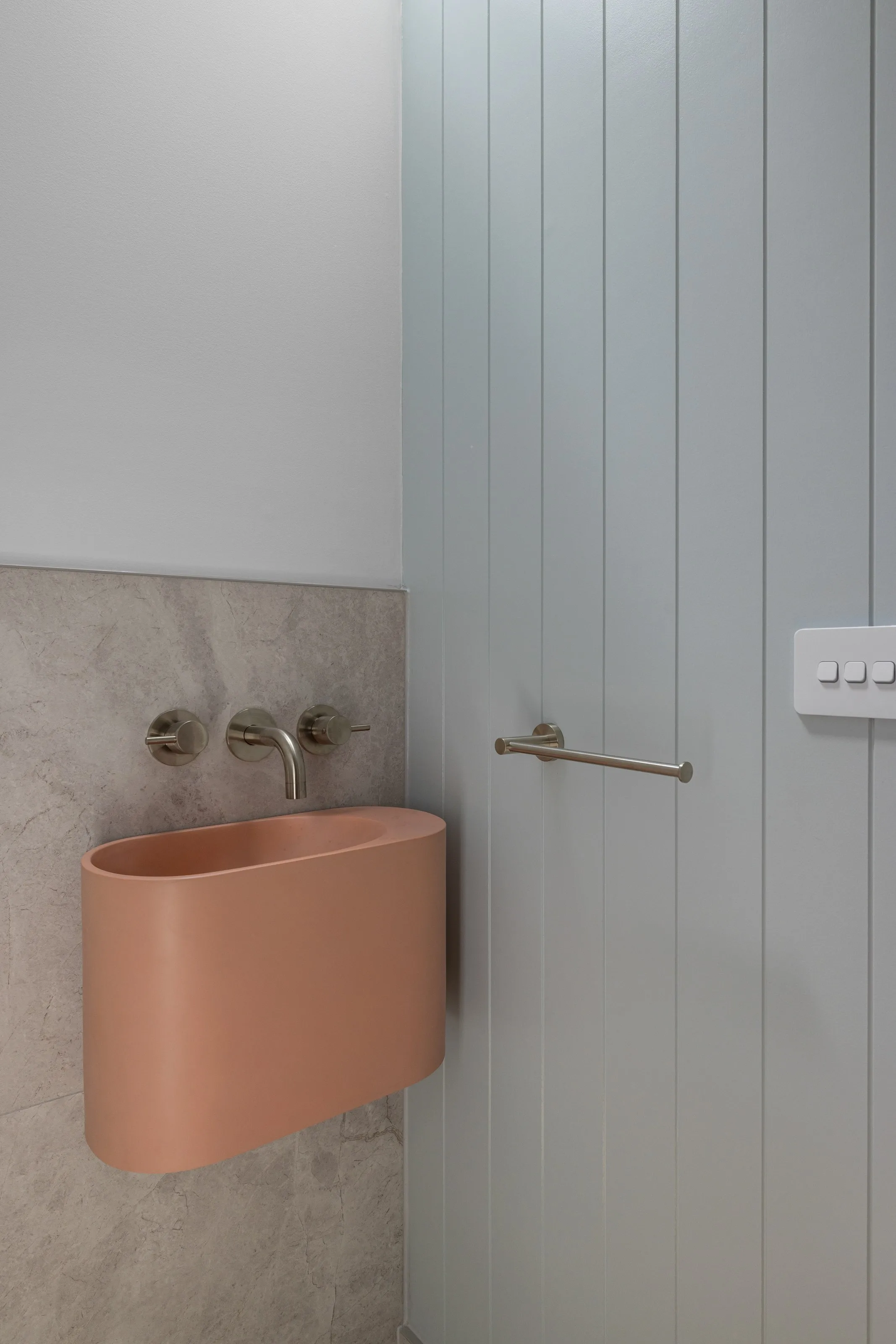 Wall-hung terracotta basin with brushed nickel tapware beside a pale VJ panelled door