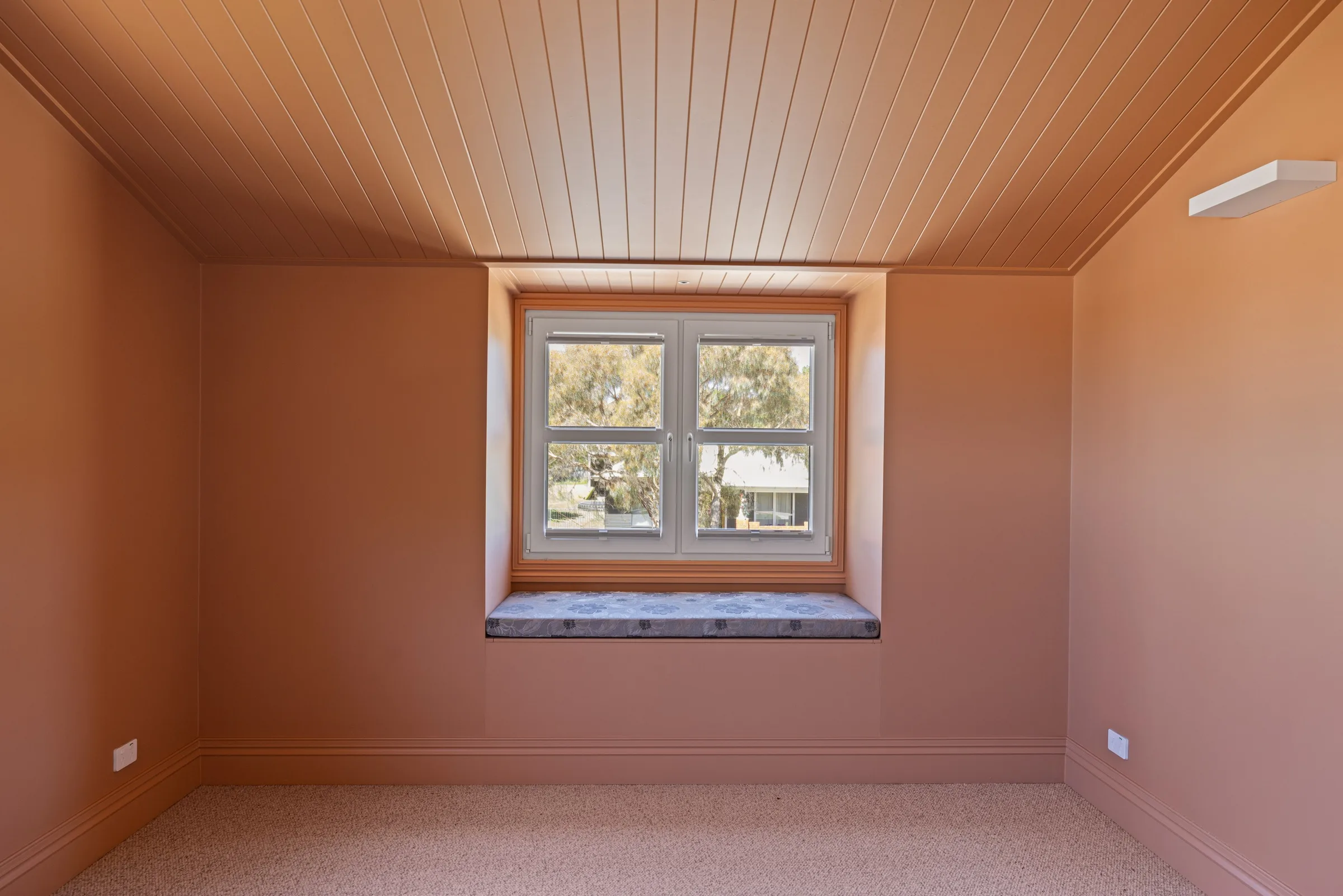 Bedroom with terracotta walls, a natural lined timber ceiling and a cushioned window seat