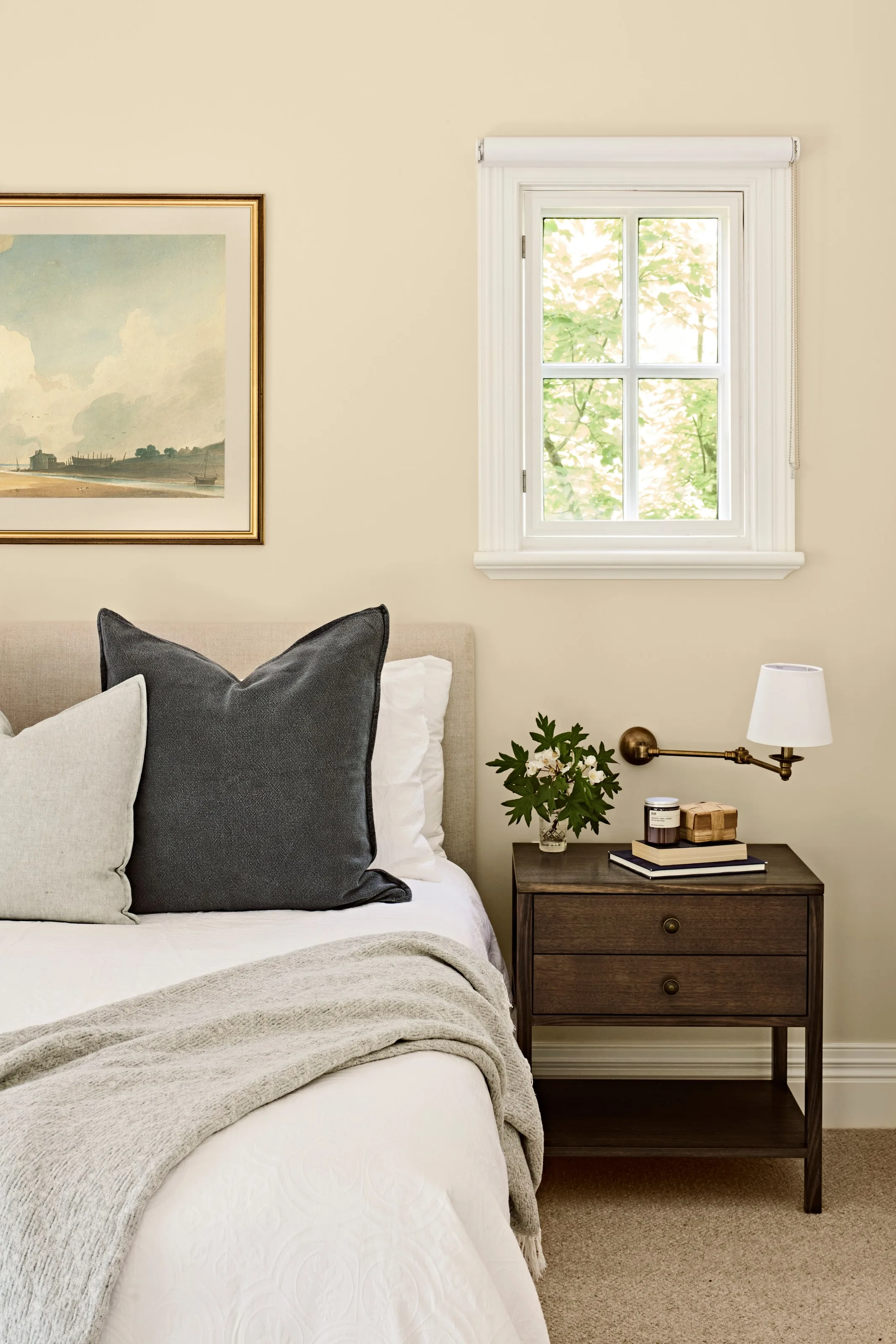 Bedside detail with brass swing-arm light, timber drawers and a small square window