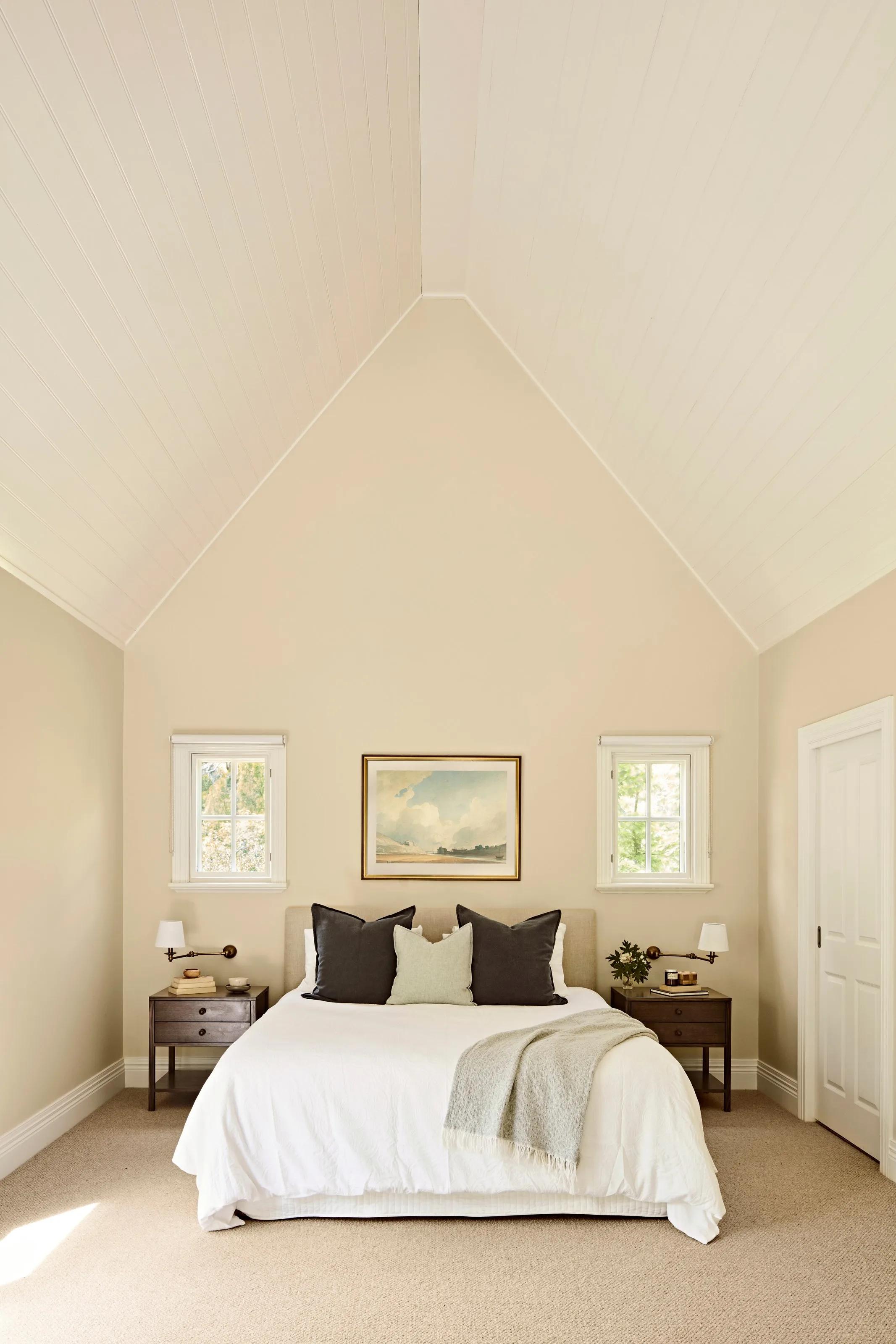 Bedroom under a soaring raked ceiling lined in painted boards, twin windows flanking the bed