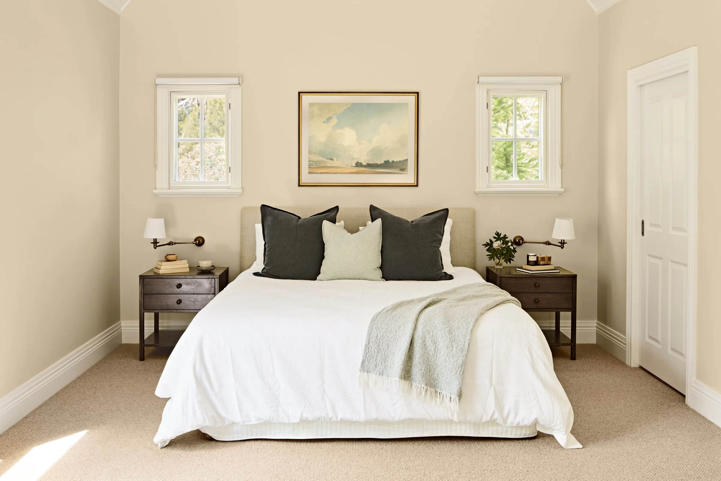 Bed centred between two small windows, seascape print above the upholstered bedhead