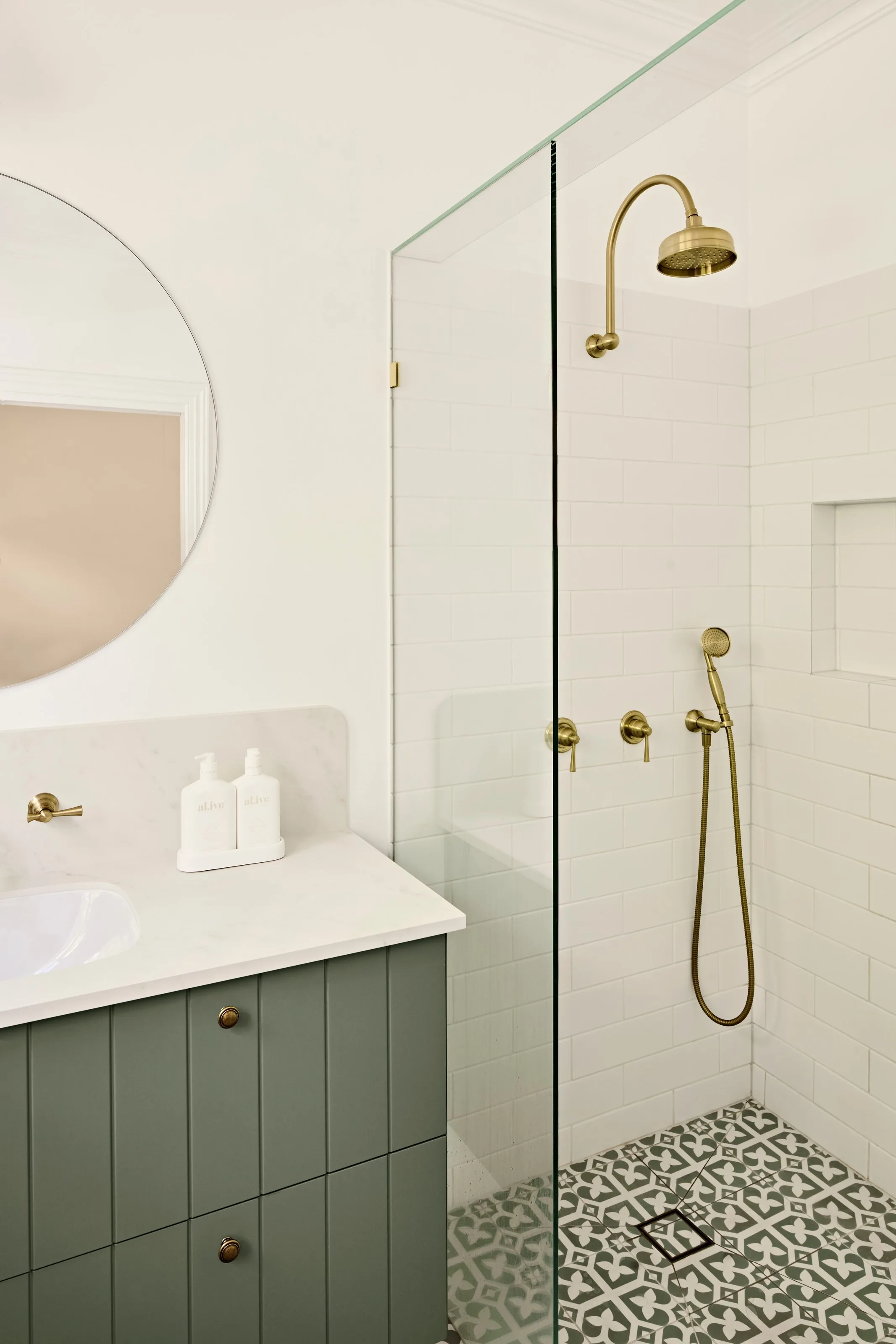 Brass rail shower over patterned tiles, white subway walls and a recessed niche