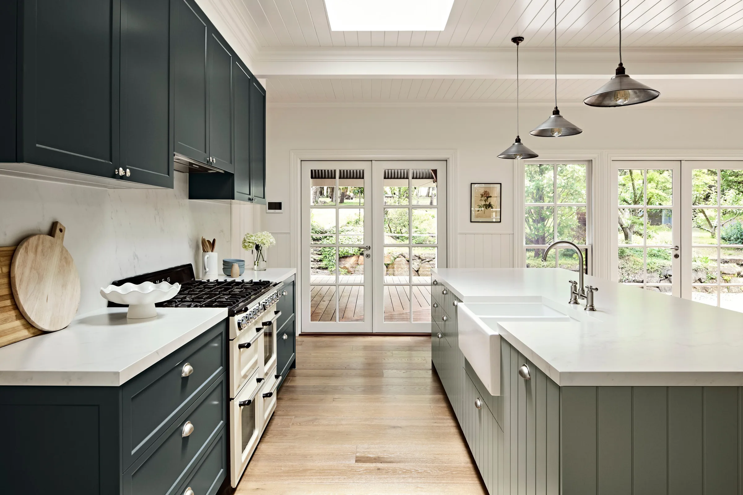 Galley run of dark joinery facing a green island with farmhouse sink and garden doors