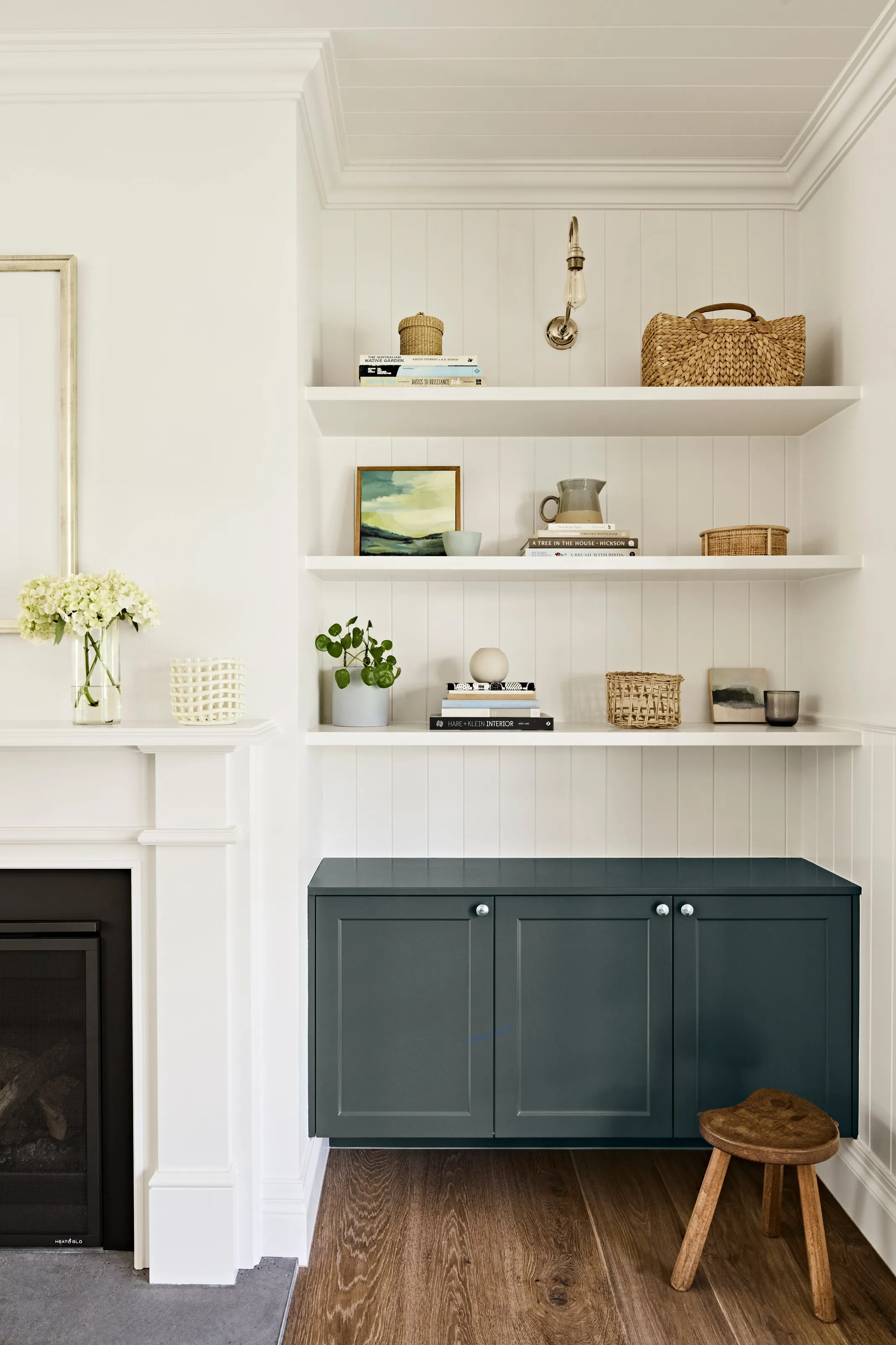 Styled floating shelves above a deep green cupboard beside the fireplace