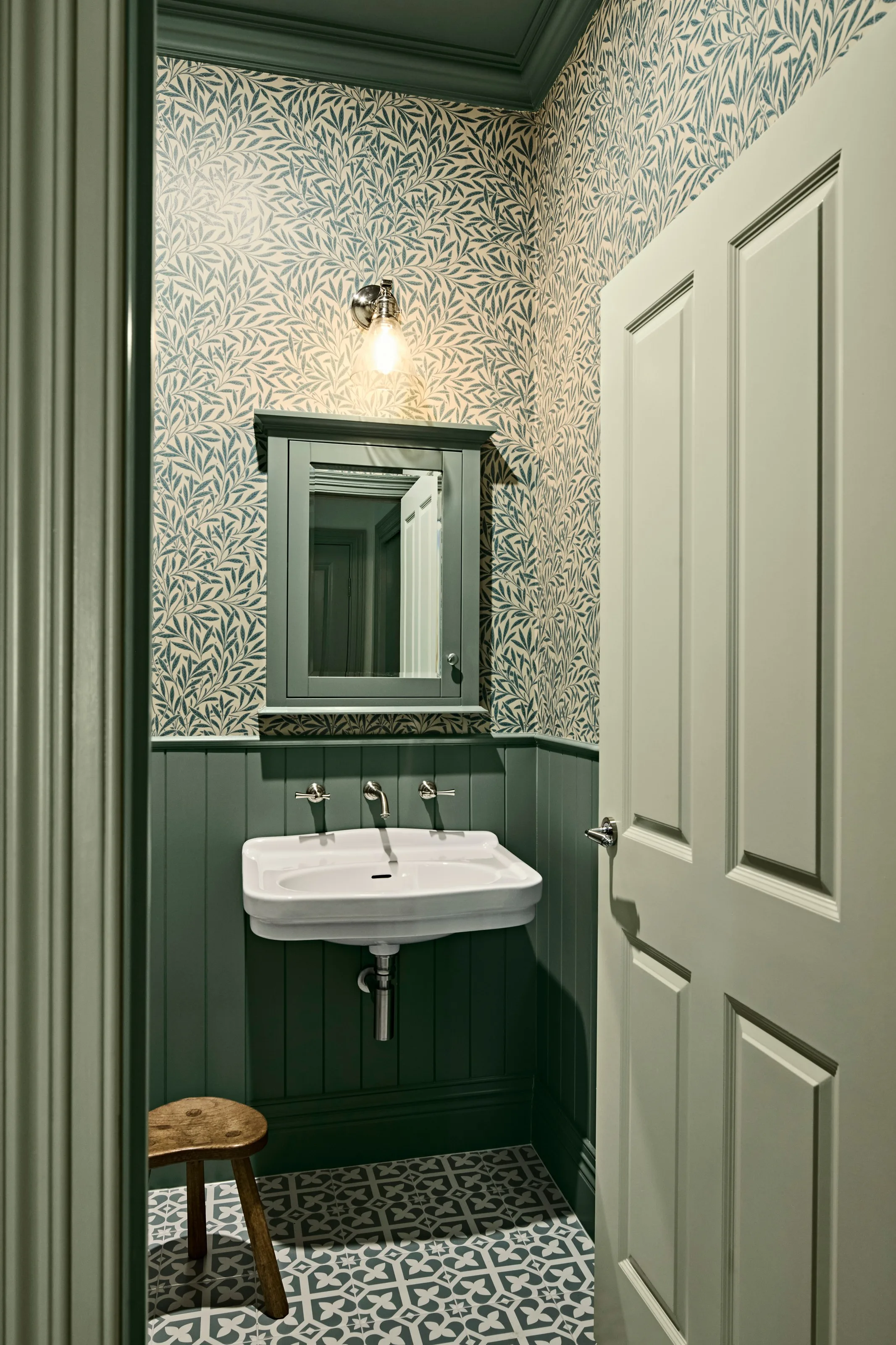 Powder room with leafy wallpaper, deep green panelling and a wall-hung basin