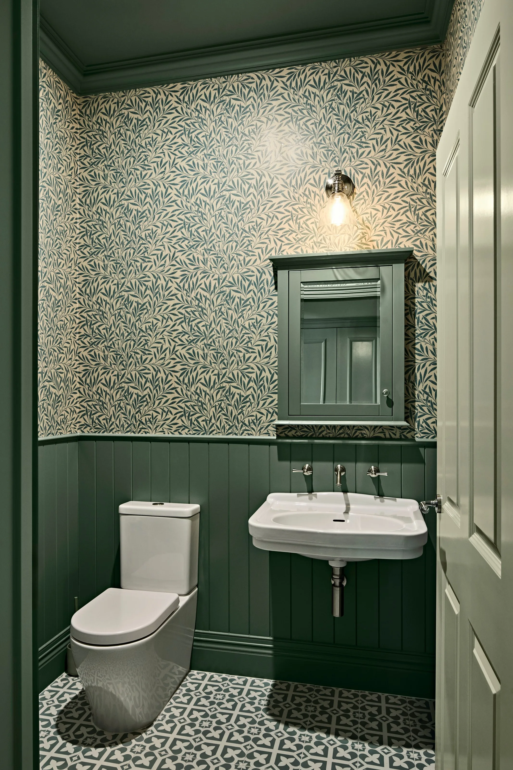 Wall-hung basin and toilet against green wainscoting under patterned wallpaper