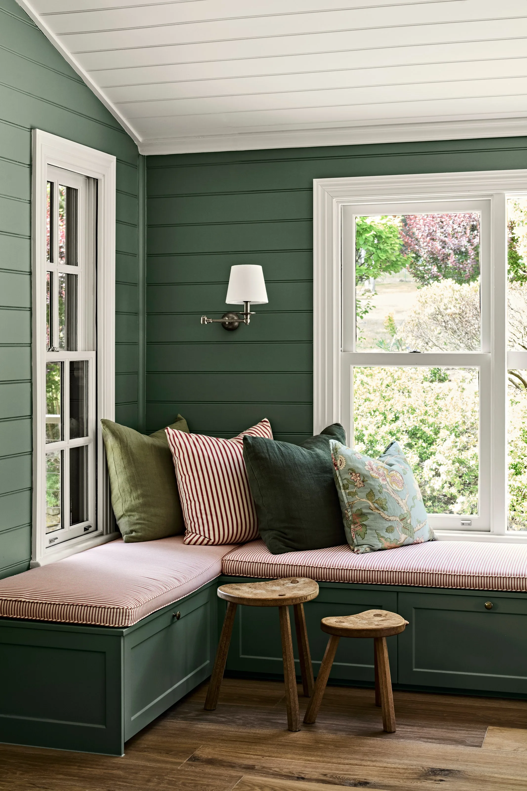 Cushioned corner seat below a sash window looking onto blossom in the garden
