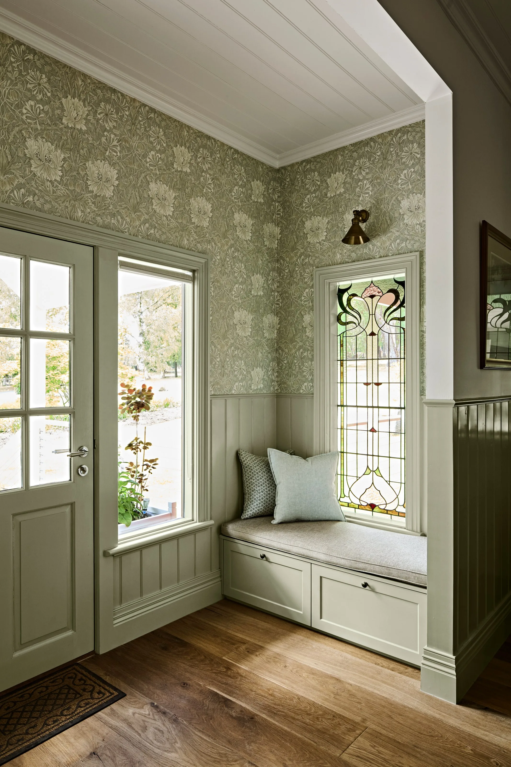 Entry with floral wallpaper, sage panelling and a built-in bench beside a leadlight window