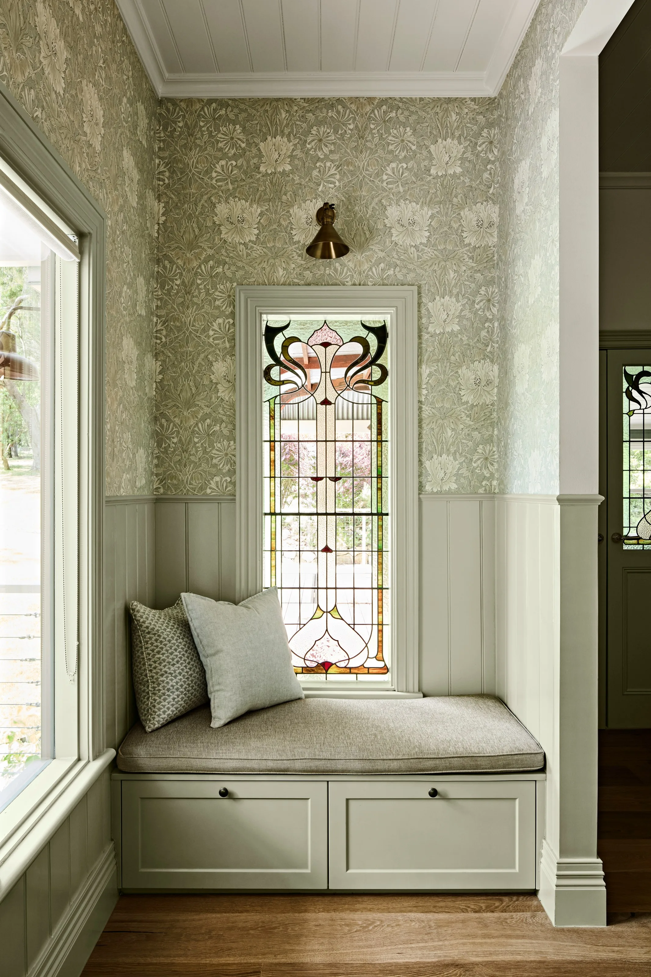 Leadlight window above a storage bench, brass wall light and patterned wallpaper