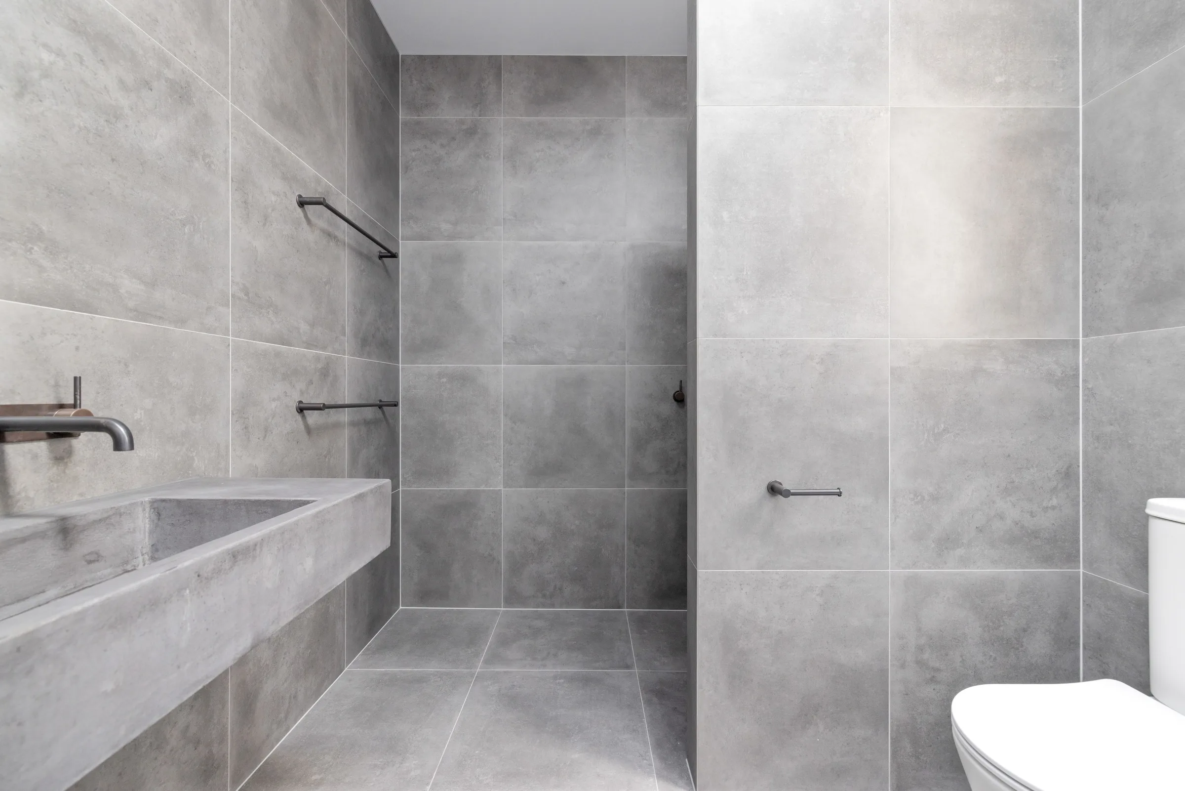 Grey tiled bathroom with a floating concrete trough basin and open walk-in shower