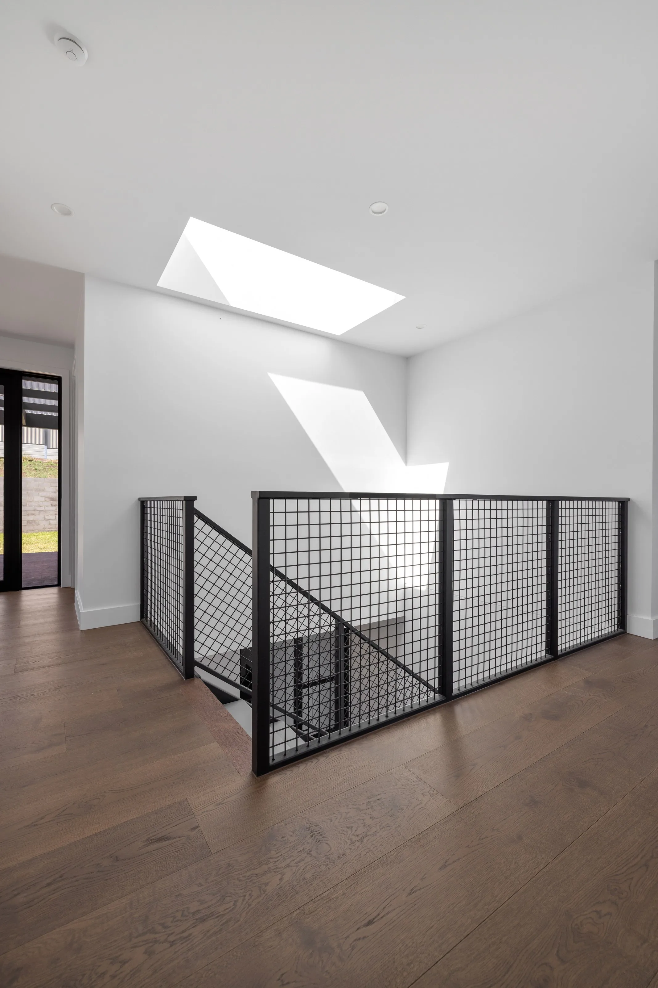 Skylight washing light across the upper landing above a black mesh balustrade
