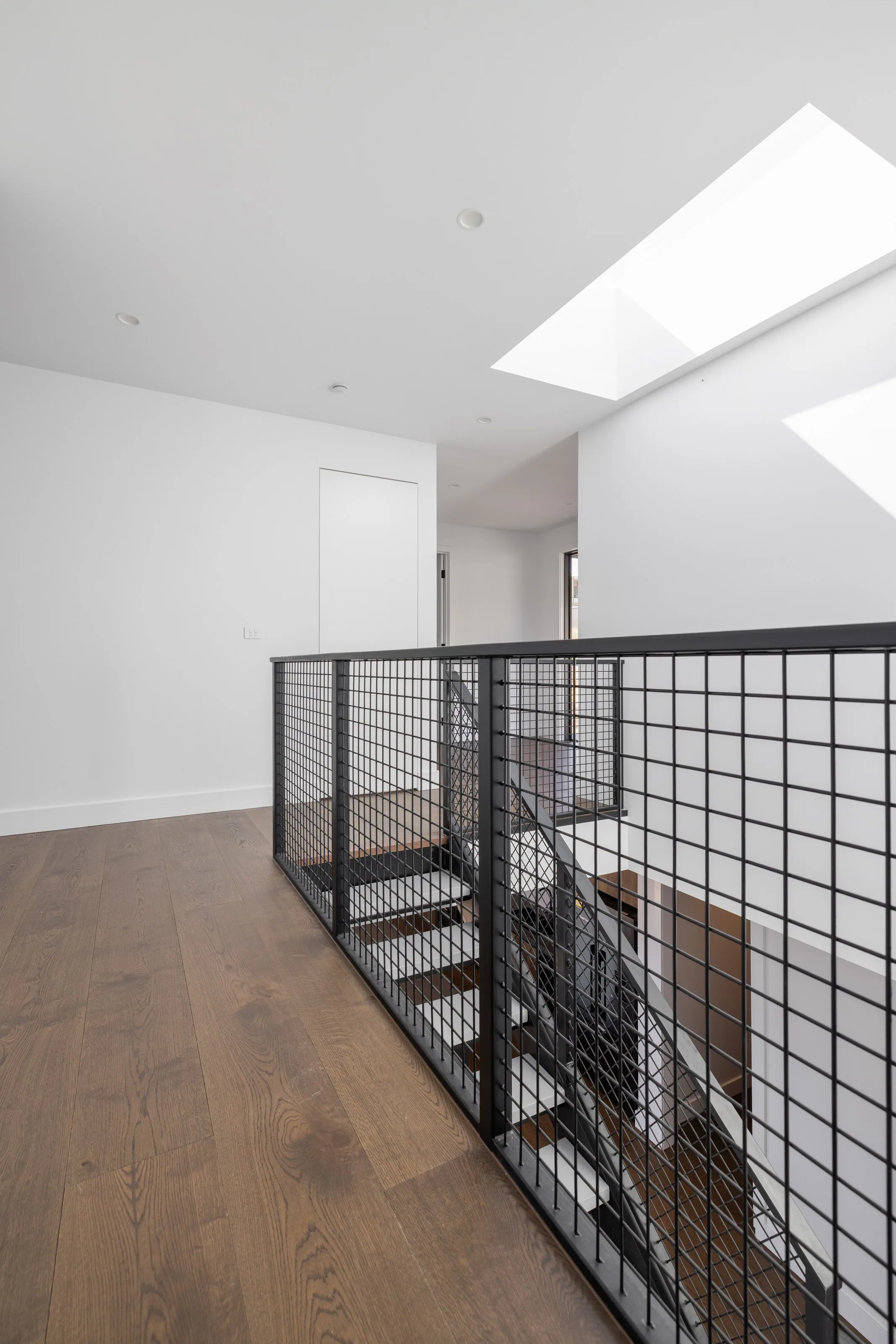 Black steel mesh balustrade edging the stair void beneath twin skylights