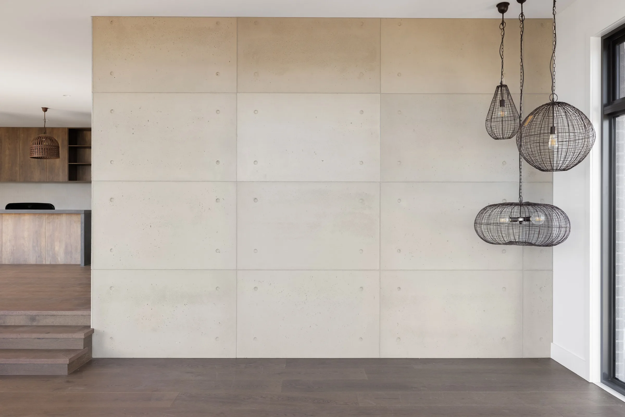 Large concrete-look wall panels beside three black wire pendants and a step down