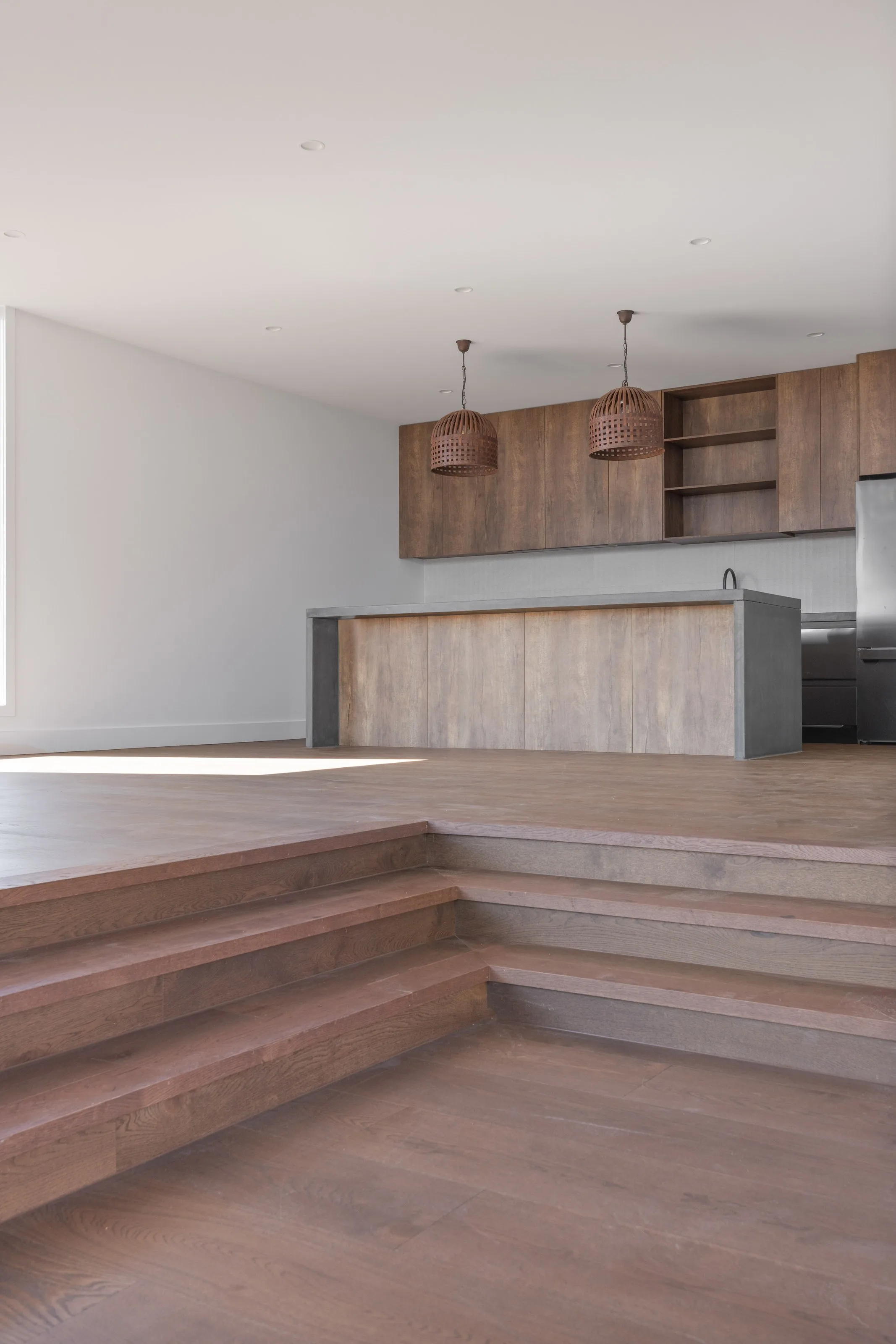 Timber steps rising from the lounge to the kitchen and its woven pendant lights