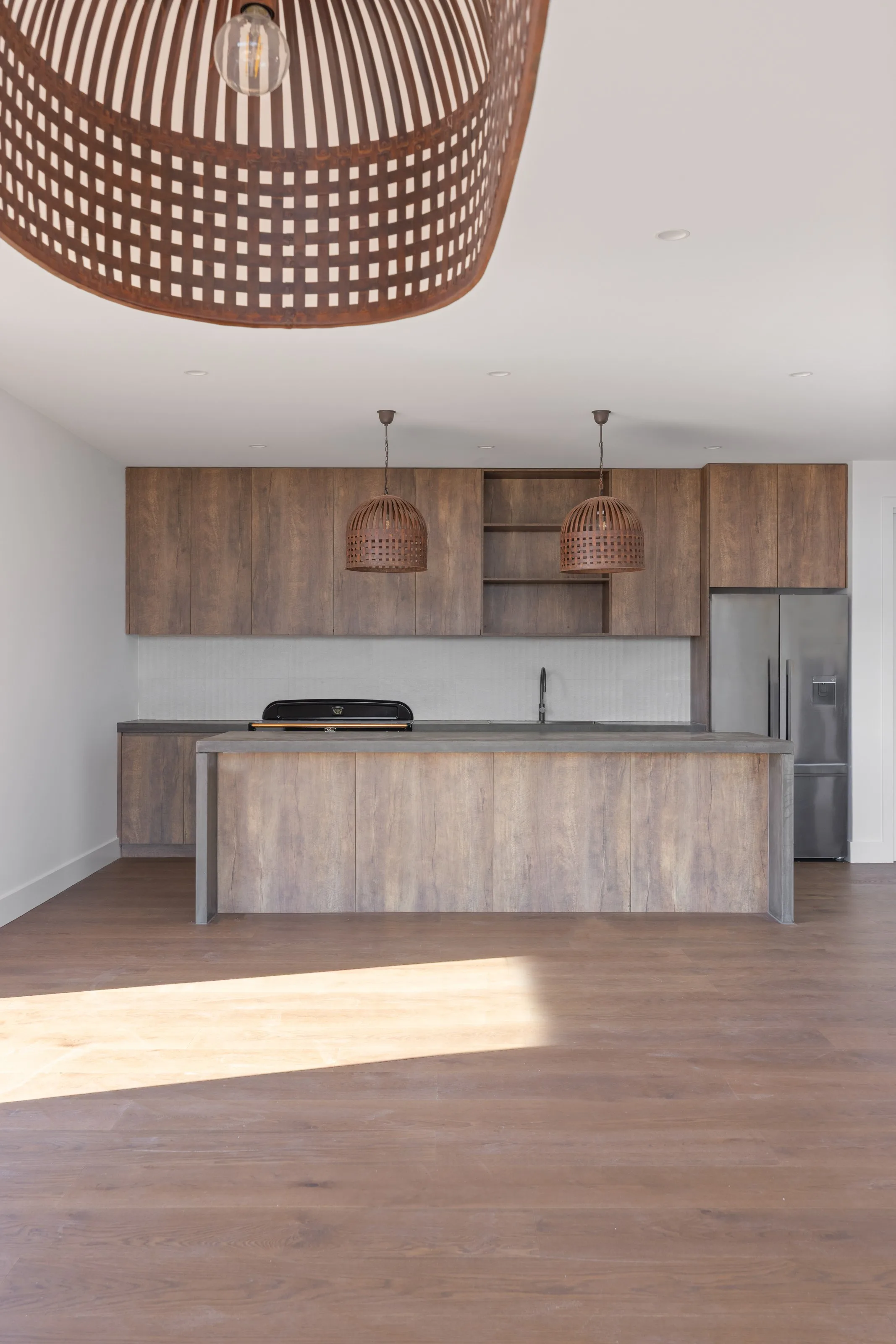 Timber-look joinery, dark benchtops and woven rattan pendants over the kitchen island