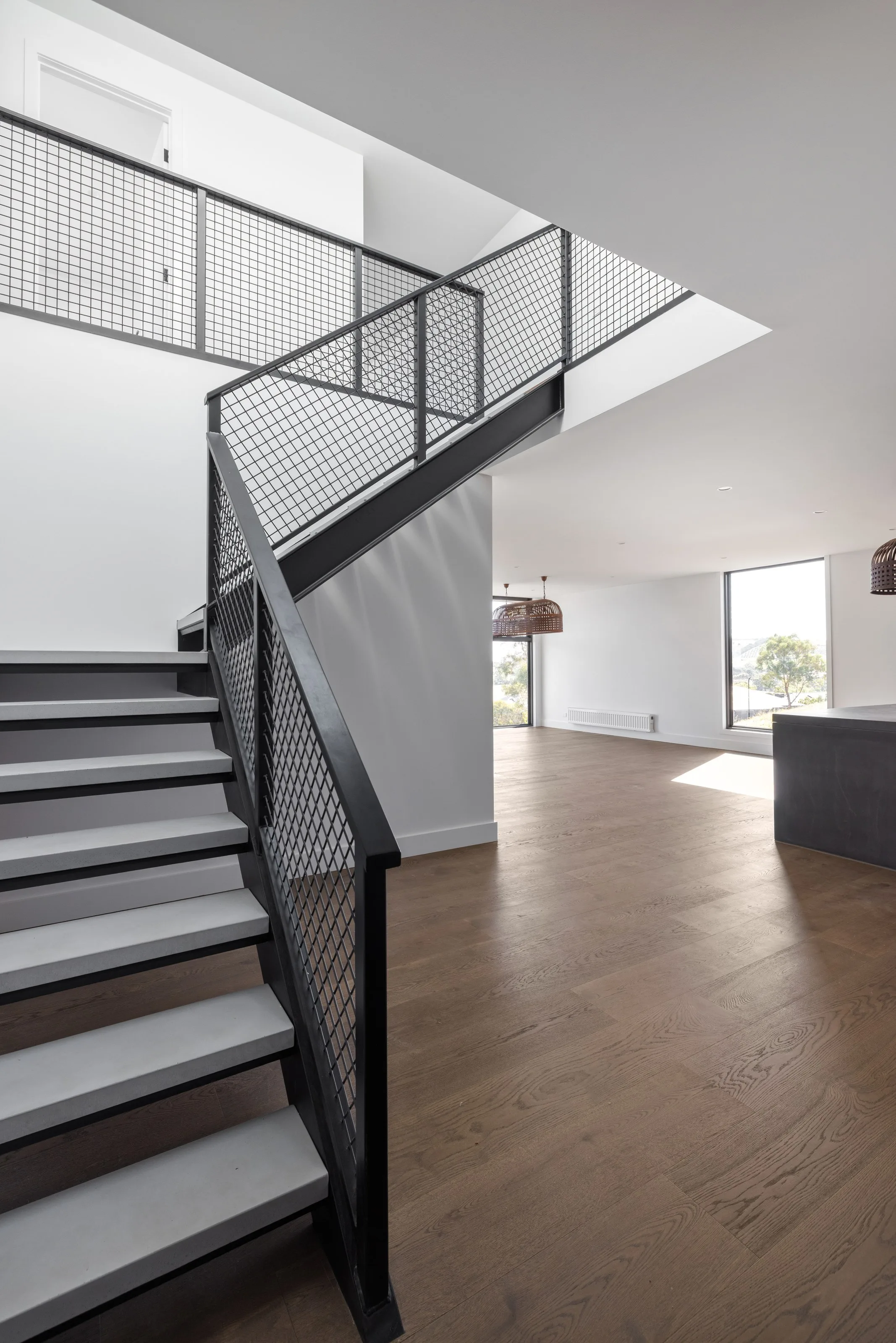 Steel stair with mesh balustrade and pale treads beside the open living area
