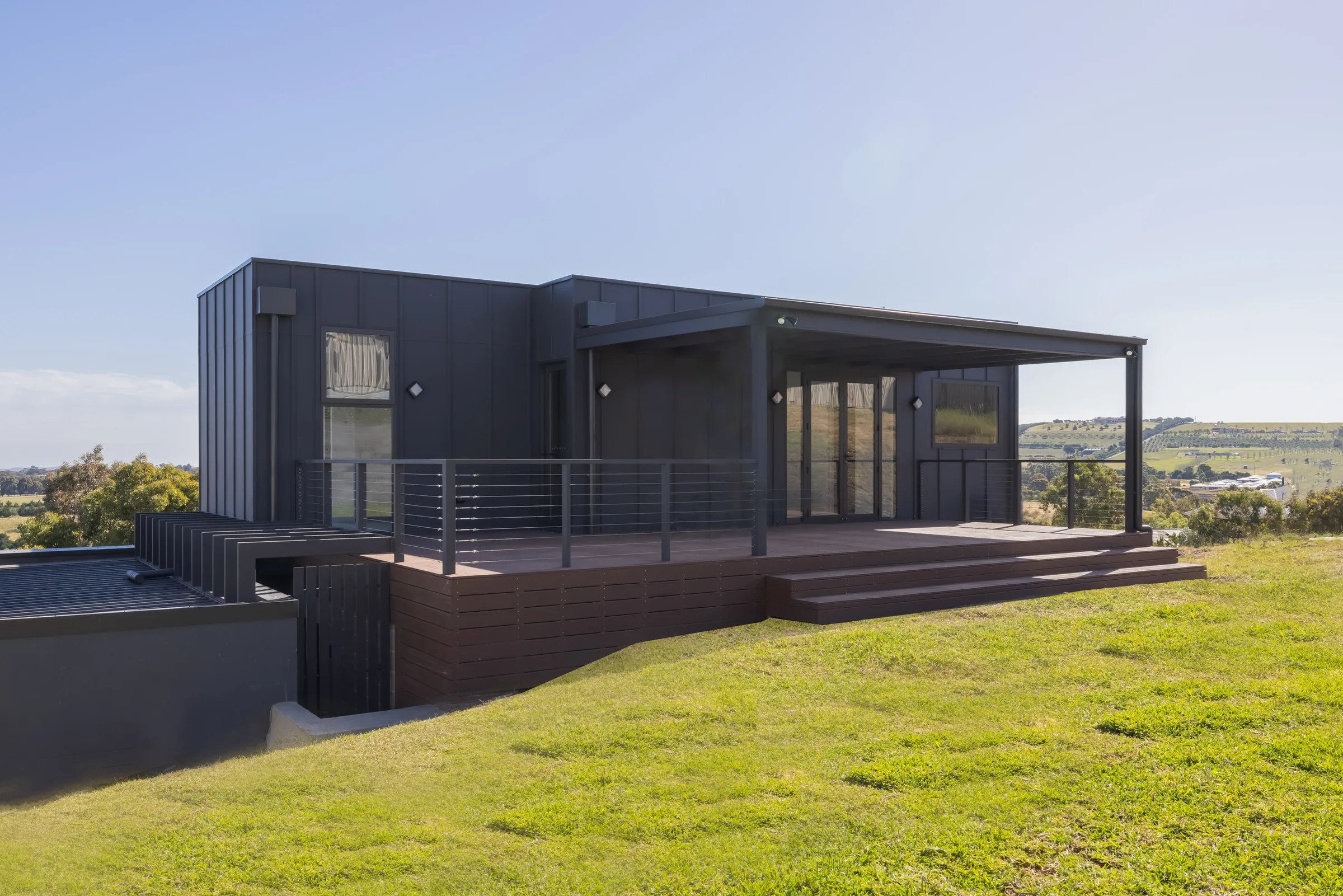 Dark clad Westminster home with a timber deck and steel balustrade above a grassy slope