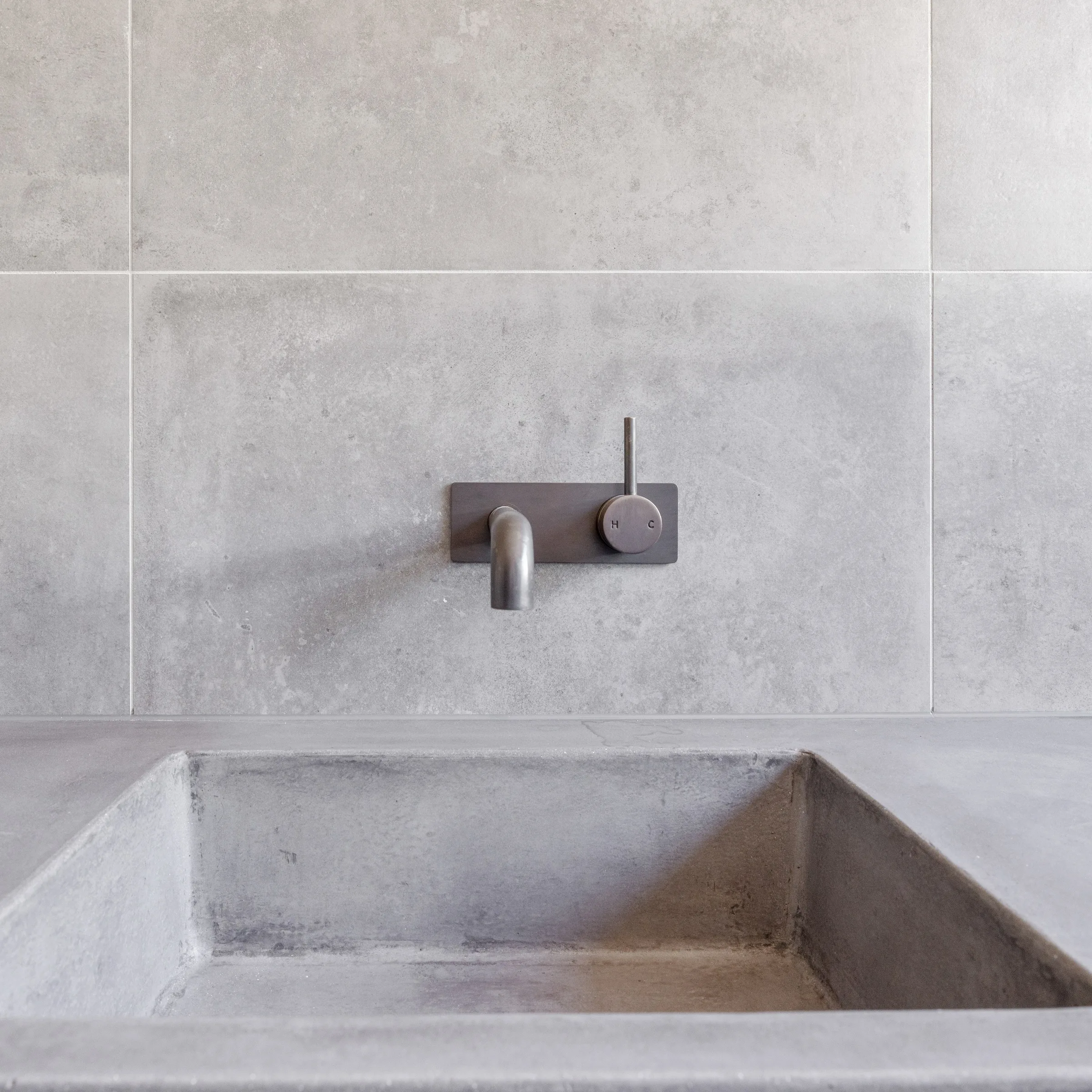 Moulded concrete basin and brushed tapware against grey tiles at Westminster