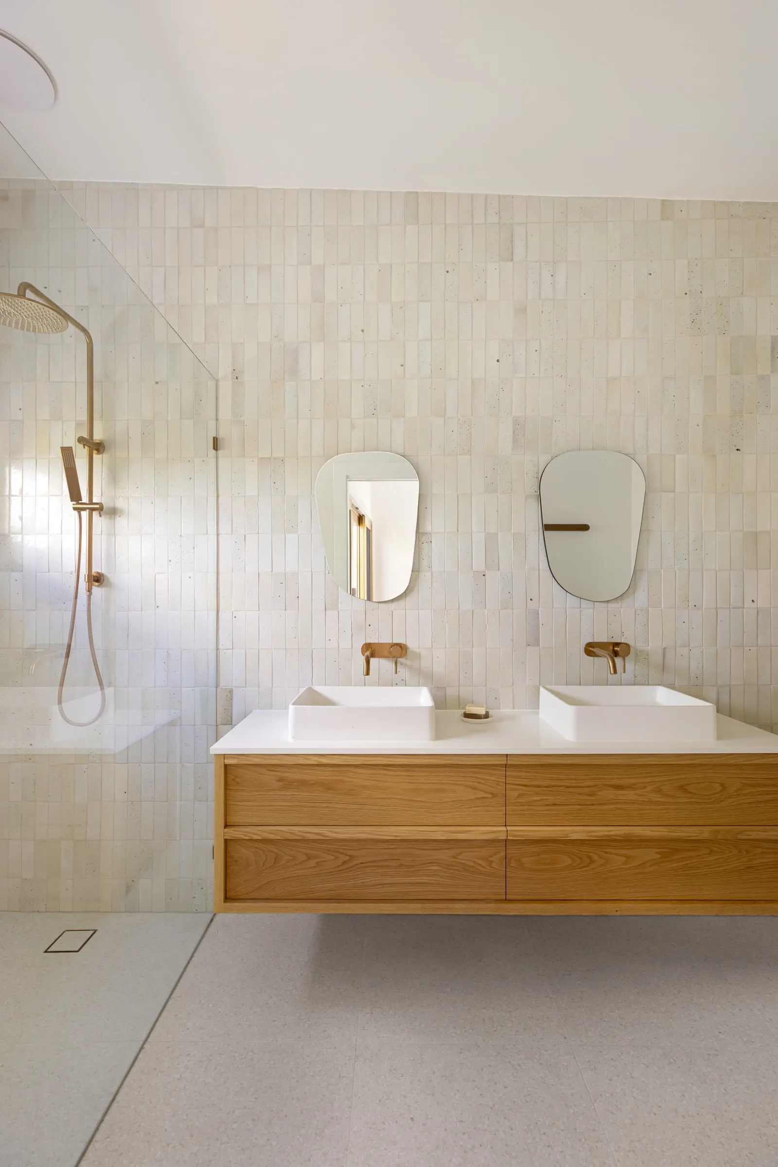 Ensuite with twin basins on an oak vanity, two mirrors and a brass rail shower behind glass