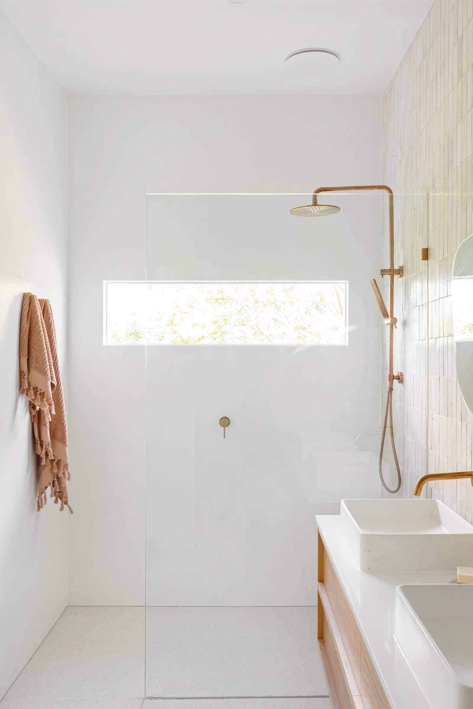 Walk-in shower with a brass rain head and a slot window looking into the garden