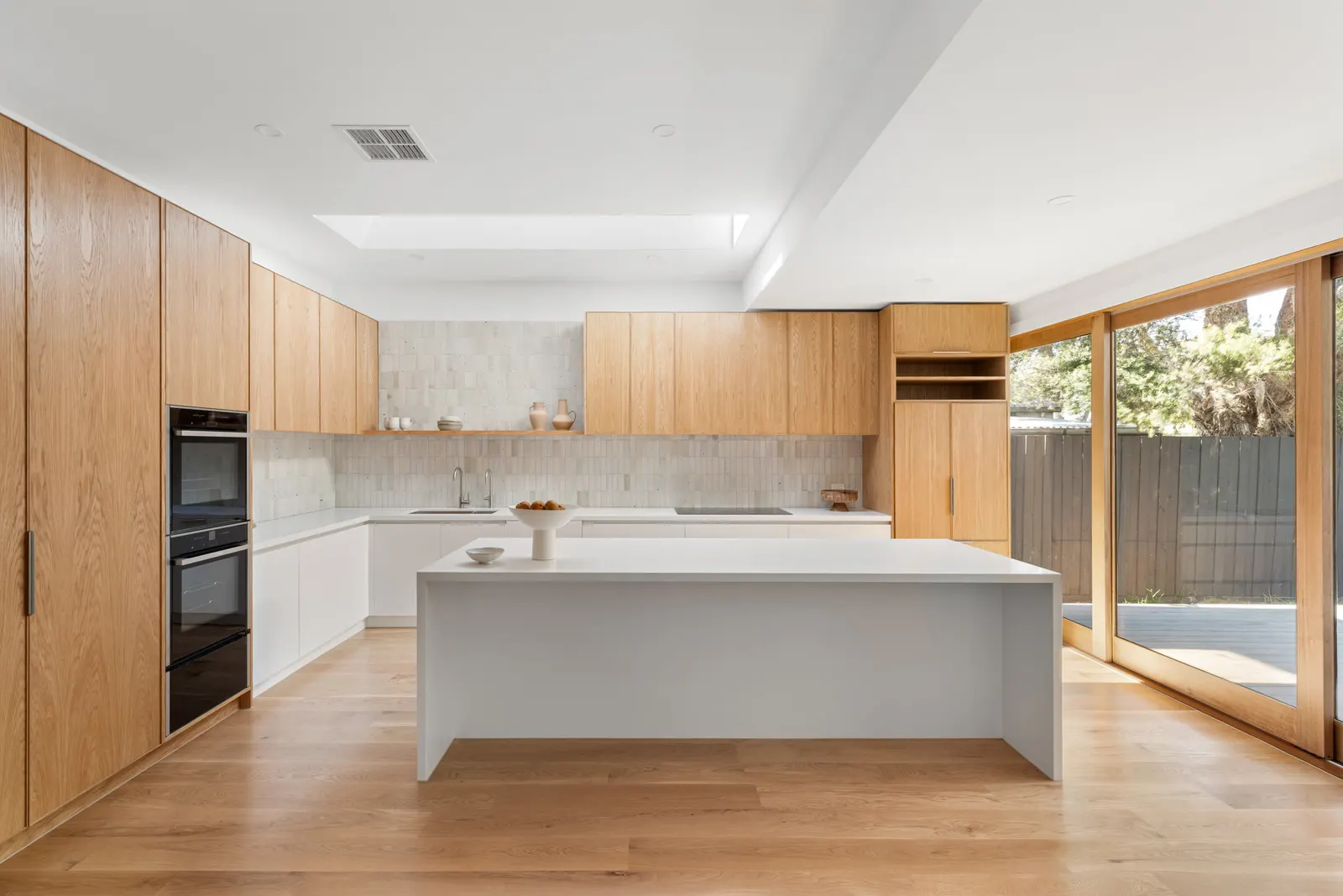 Renovated kitchen at Charles St with oak joinery, a white island and doors to the deck