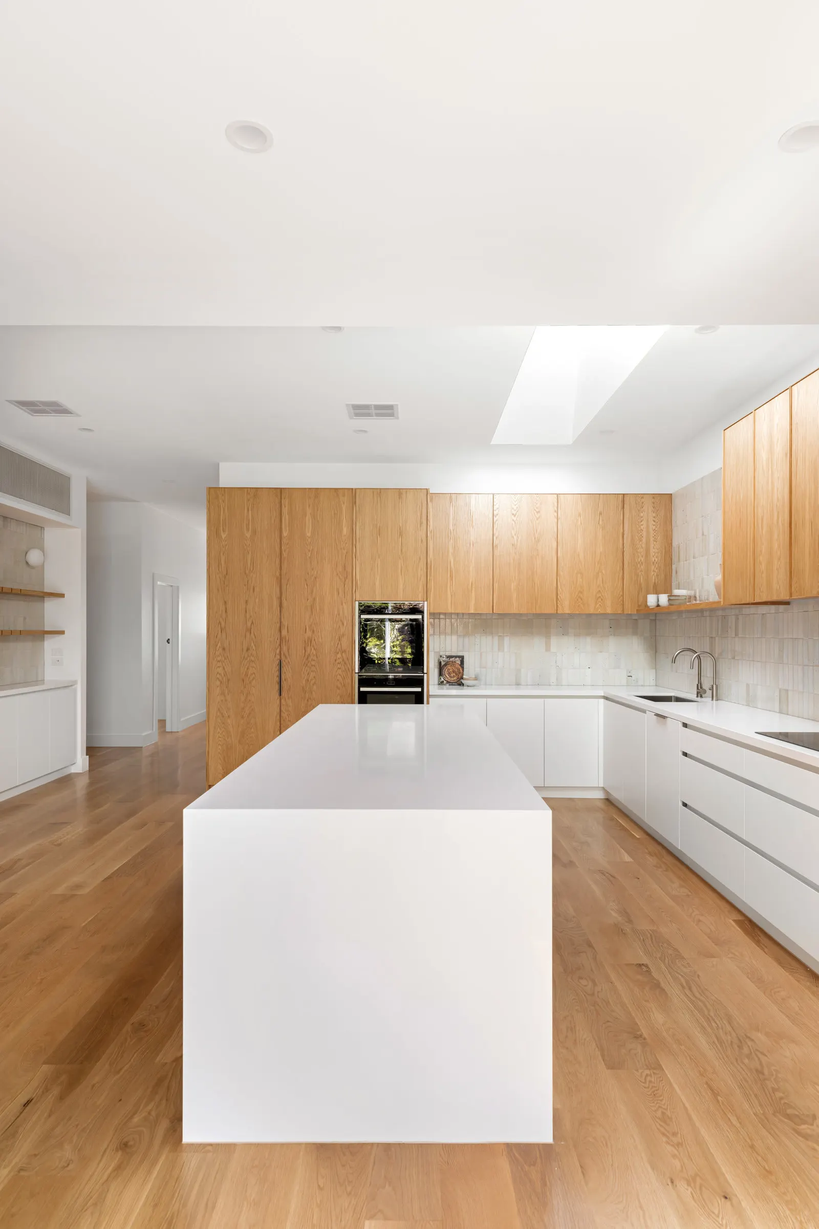 Long white waterfall island running through the kitchen beneath a skylight