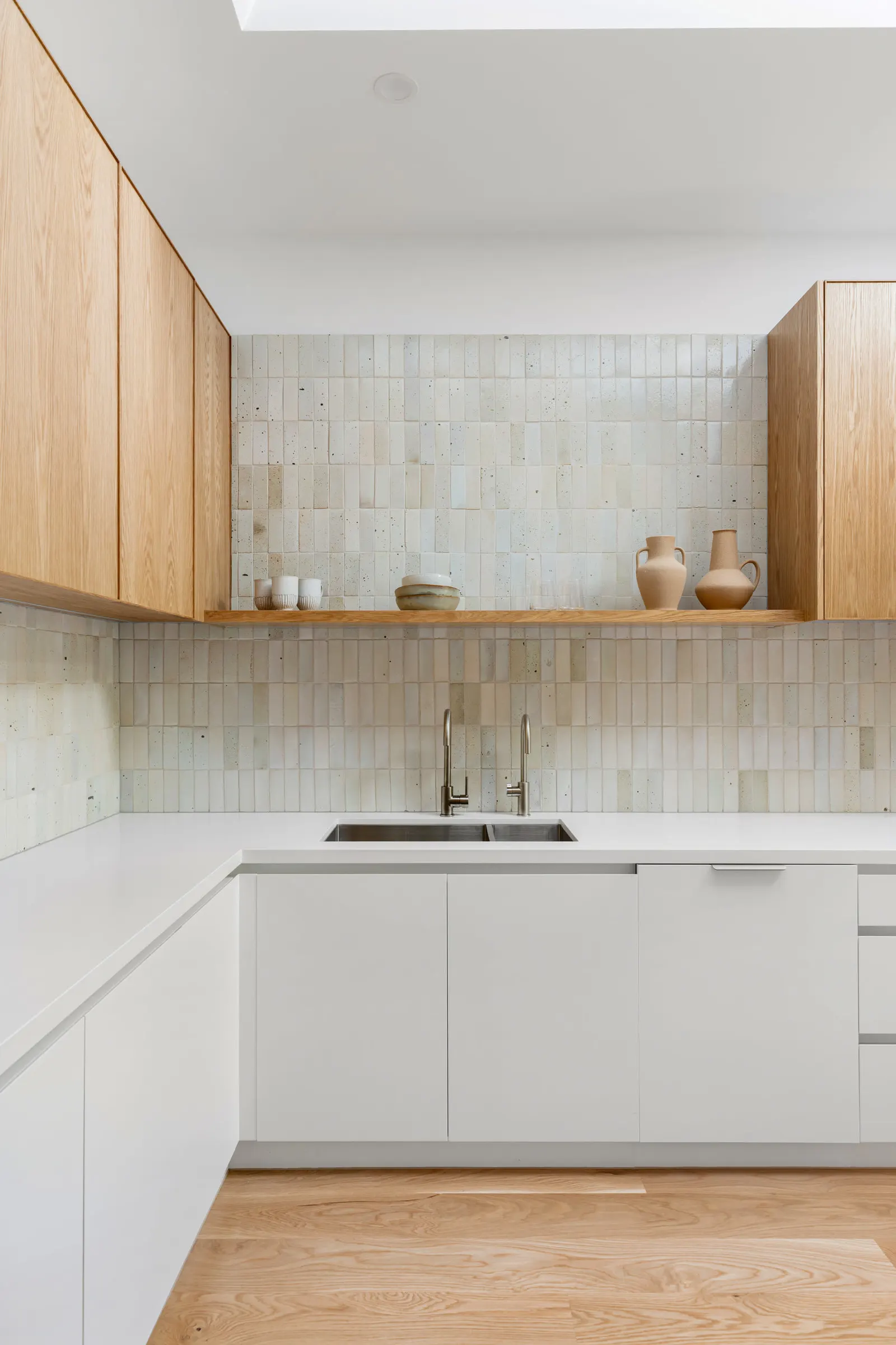 Double sink and gooseneck tapware below a timber shelf of ceramics on tiled splashback