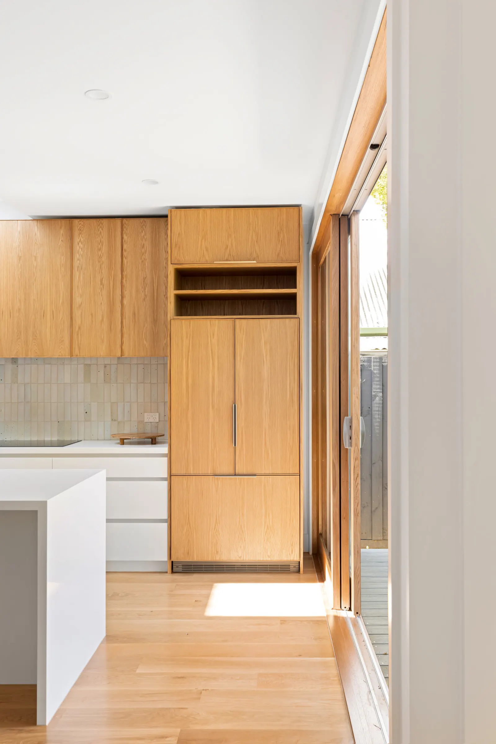 Integrated oak tall joinery beside the kitchen bench, with the deck door alongside