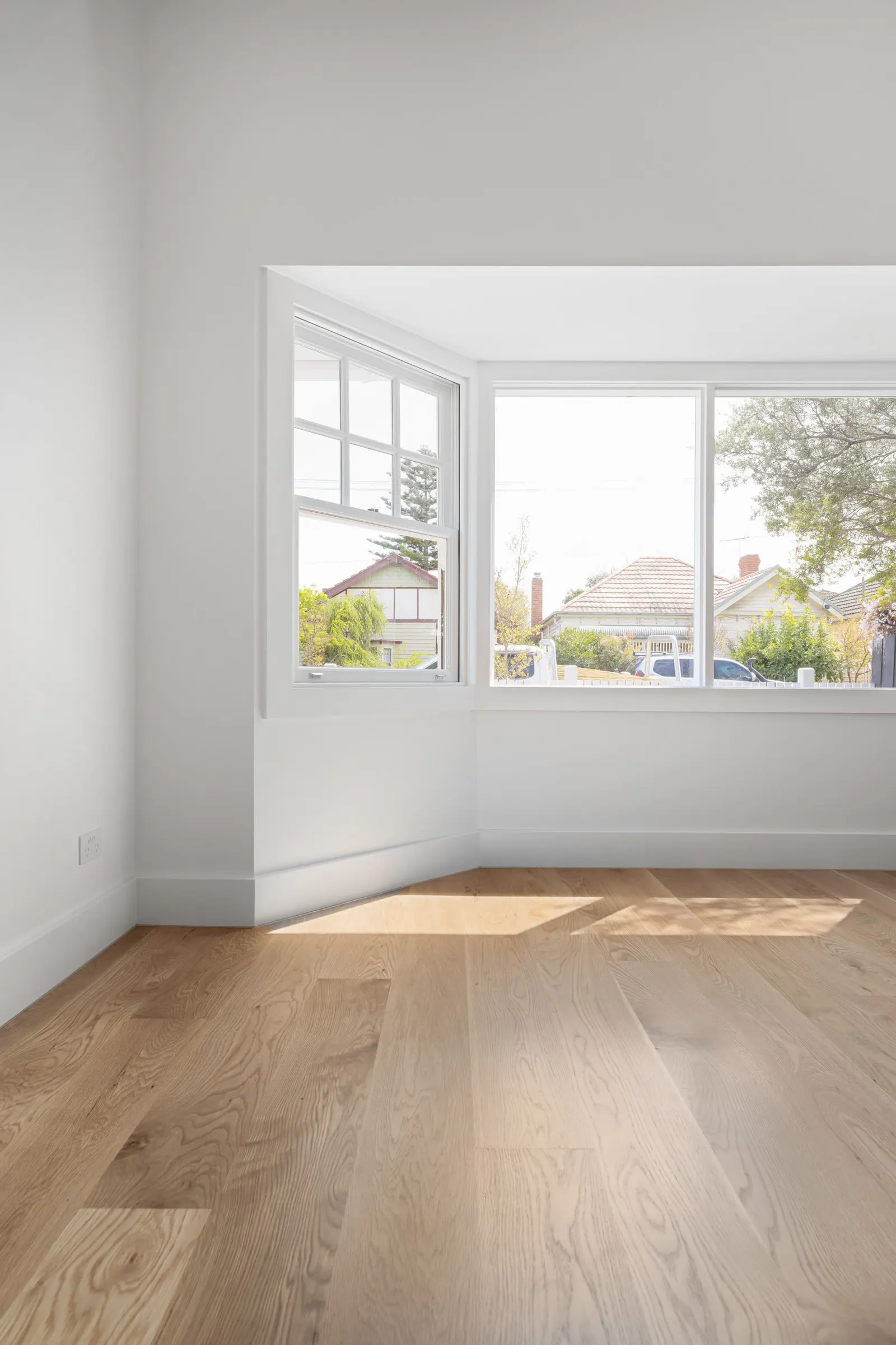 Empty front room with white-framed corner windows and oak floorboards