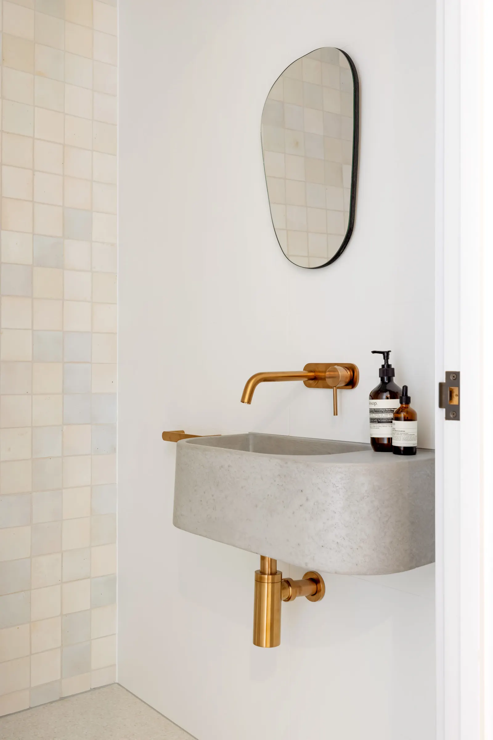 Powder room with a wall-hung stone basin, brass tapware and an oval black-framed mirror
