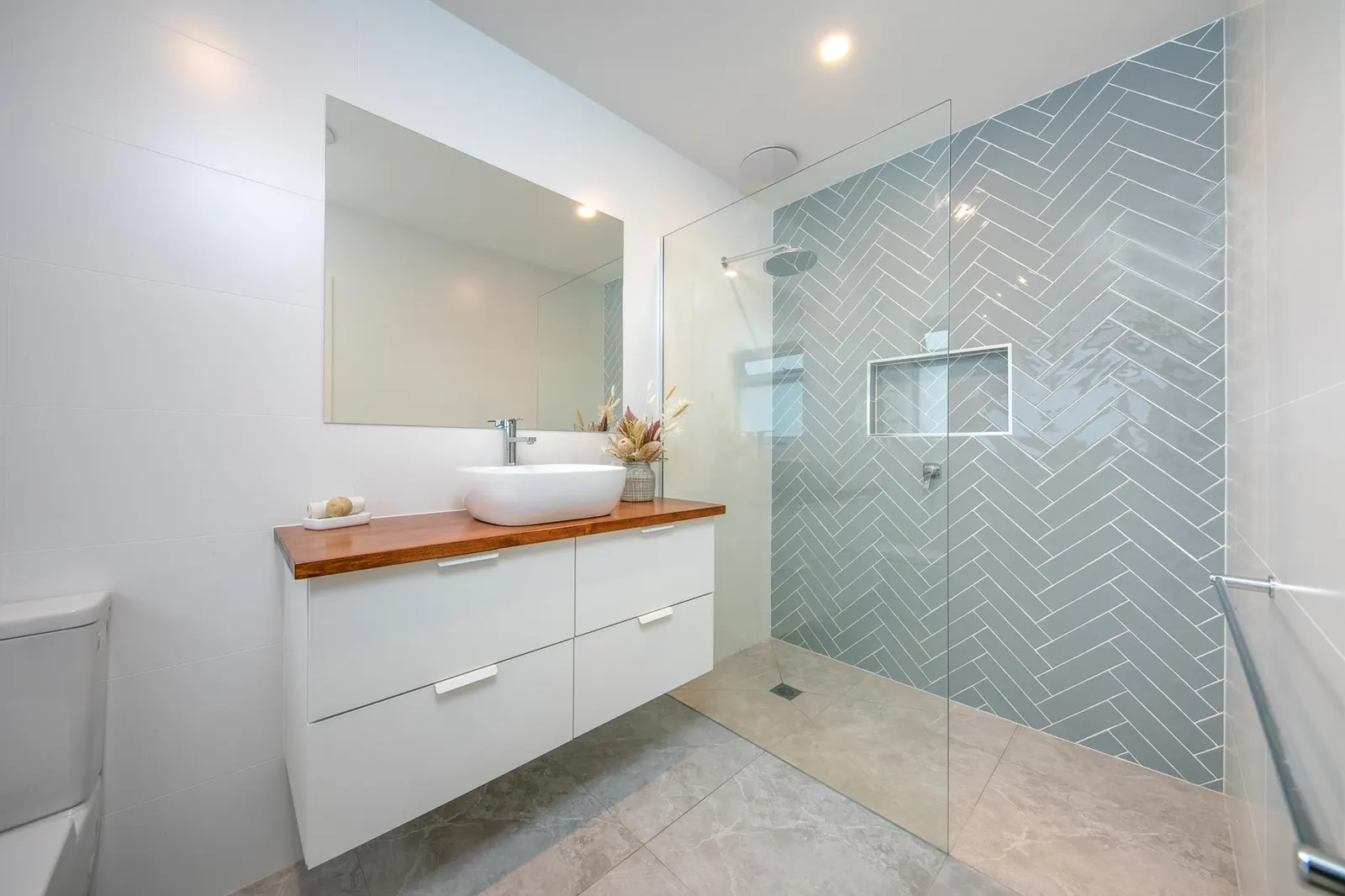 Bathroom with a white vanity, timber benchtop and vessel basin beside a blue herringbone tiled shower