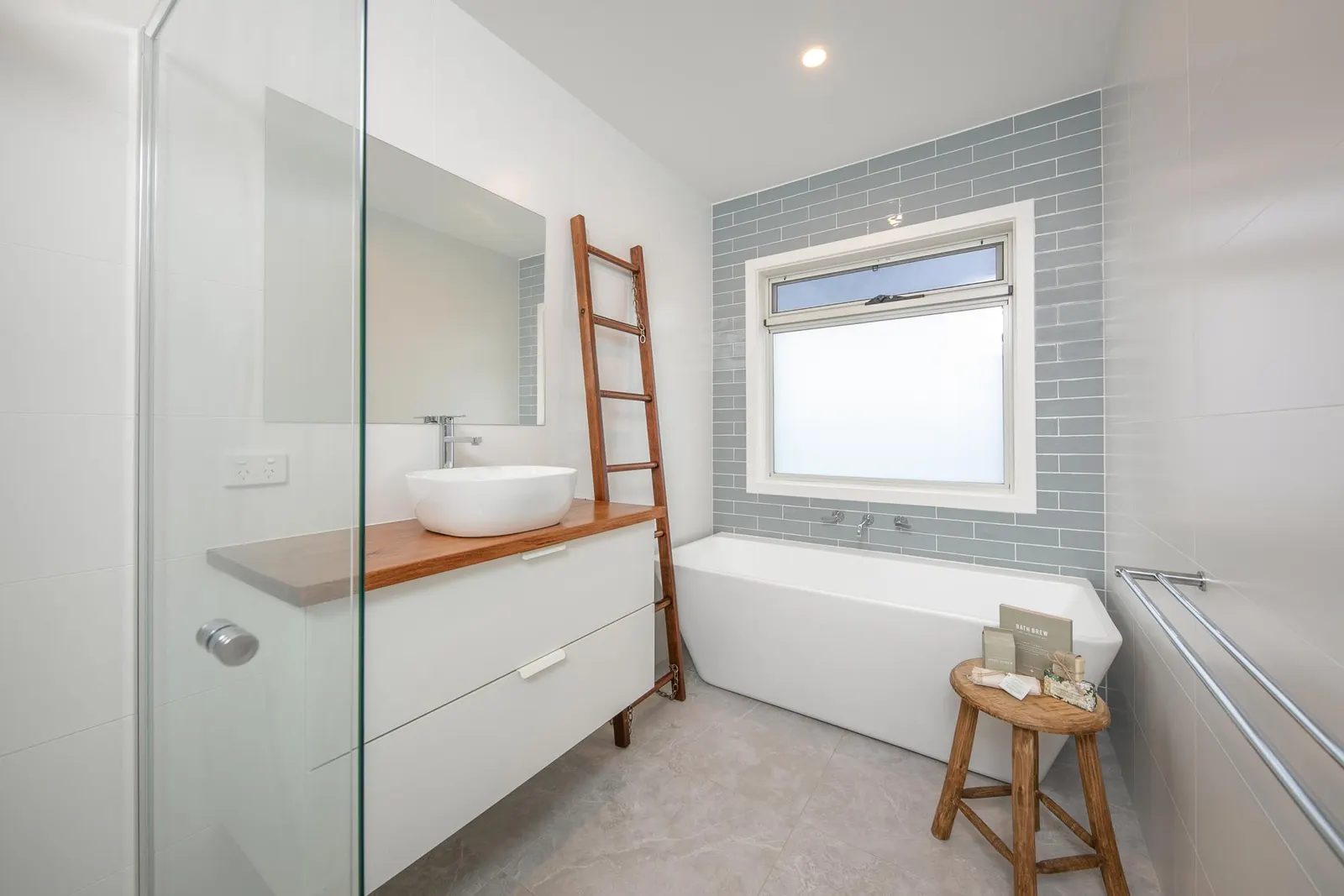 Bath set under a frosted window with blue-grey subway tiles and a timber ladder rail alongside