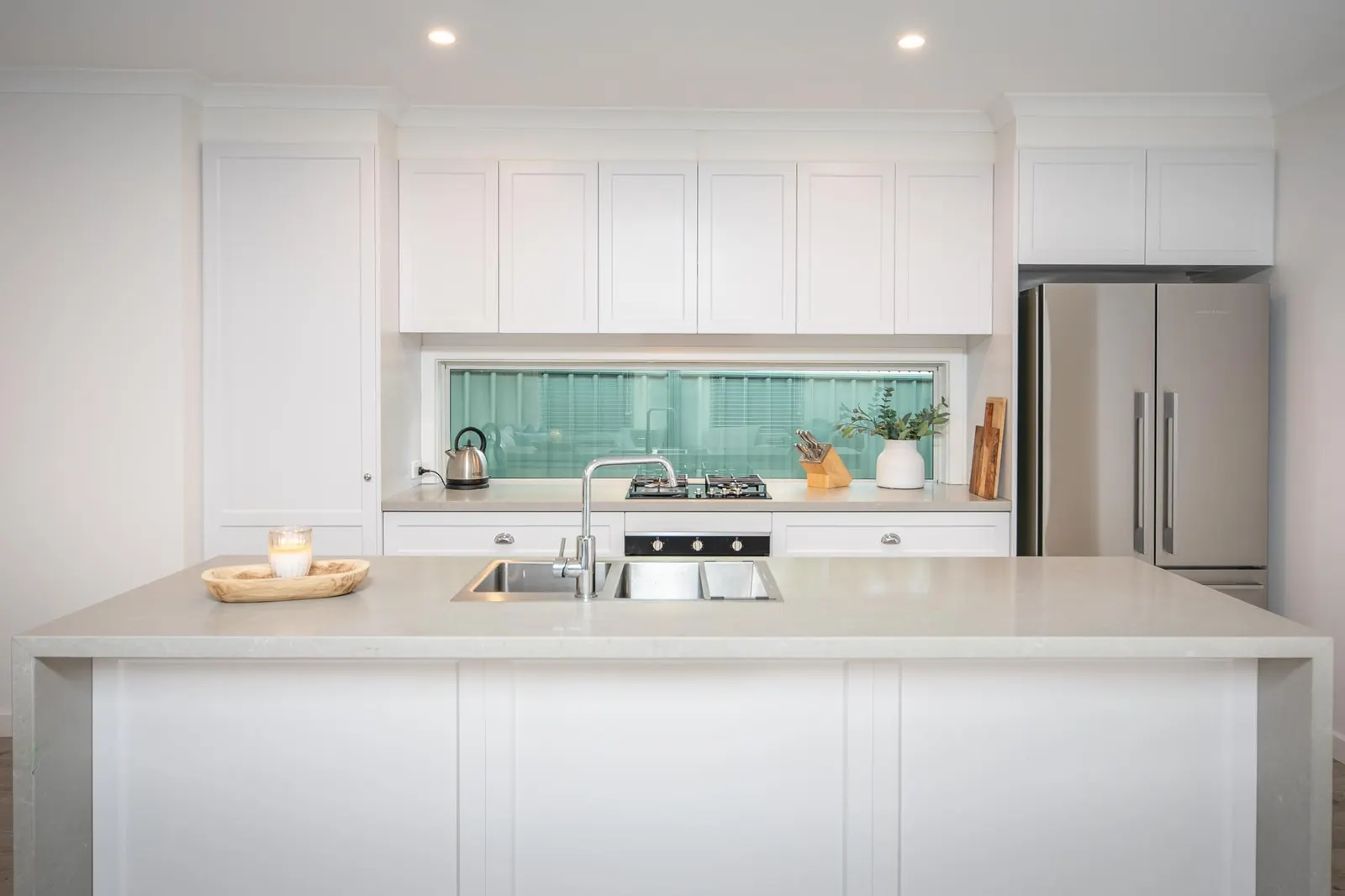 White shaker kitchen with a stone island benchtop and a green glass window splashback
